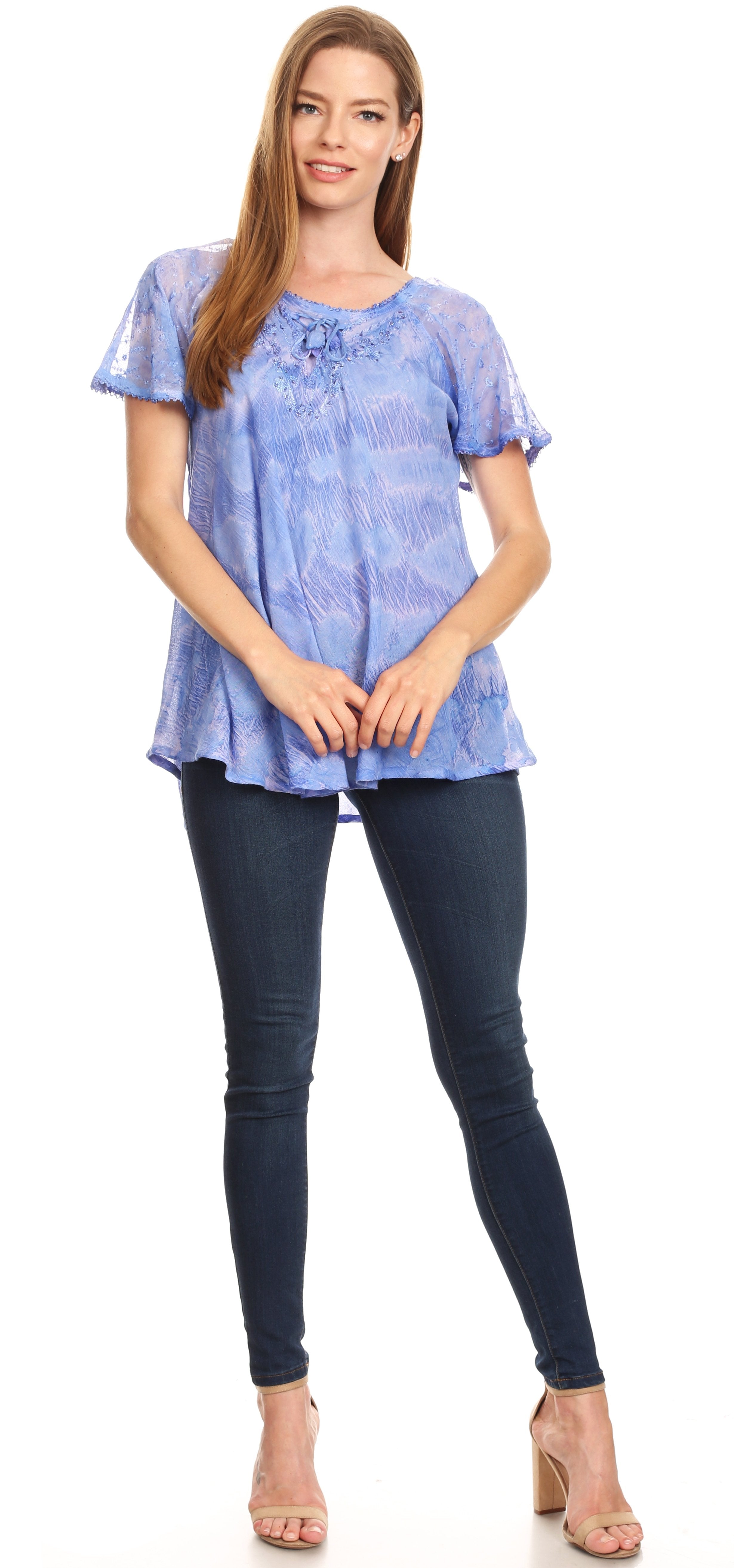 Woman wearing a blue patterned top and dark jeans on a white background