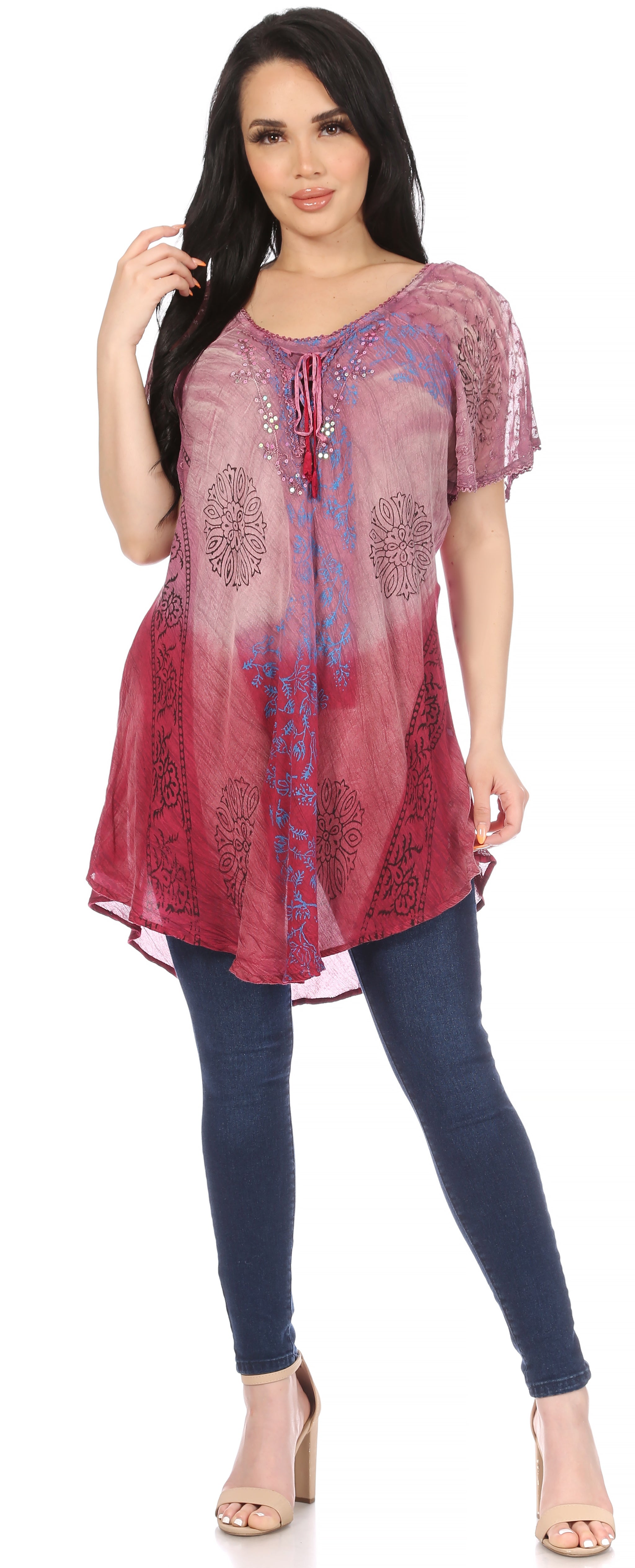 Woman wearing a patterned pink and purple top with blue jeans on a white background