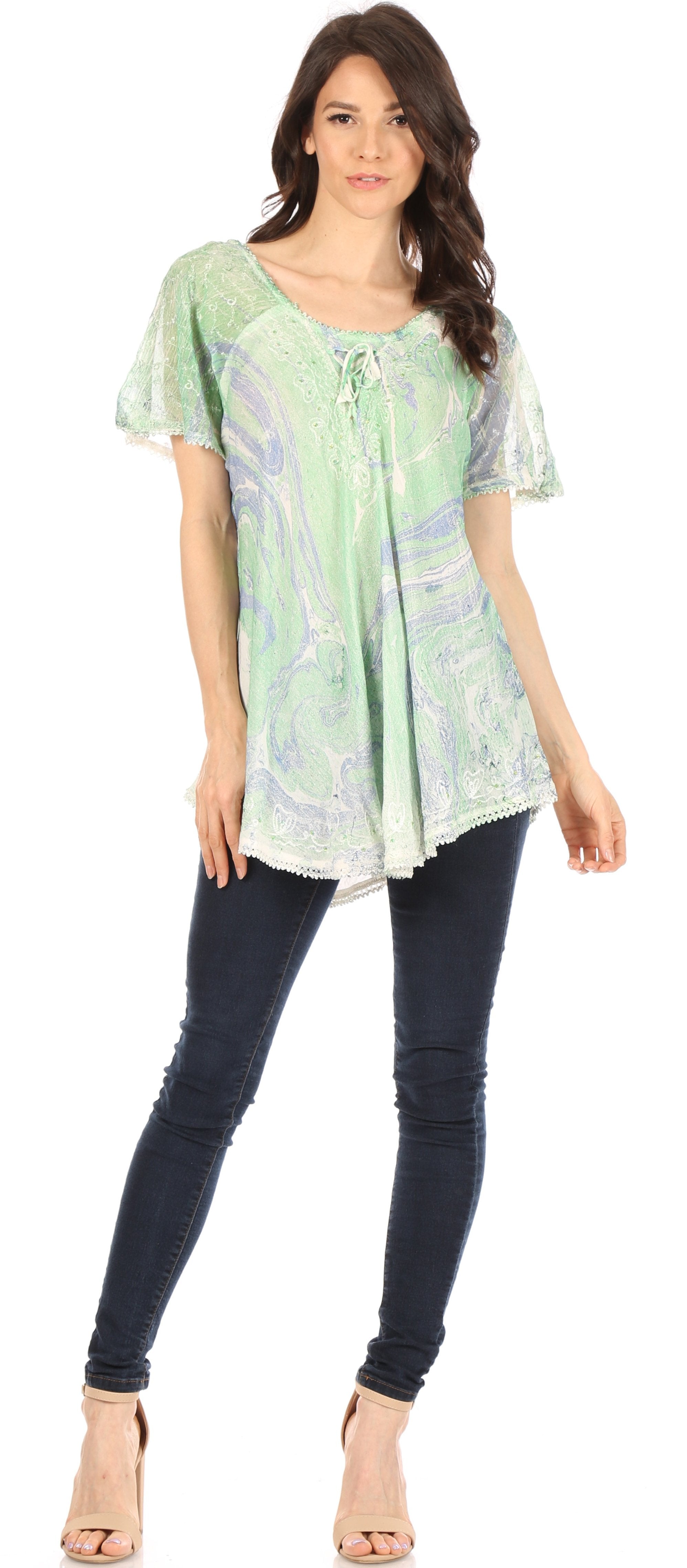 Woman wearing a light green patterned tunic and dark jeans on a white background