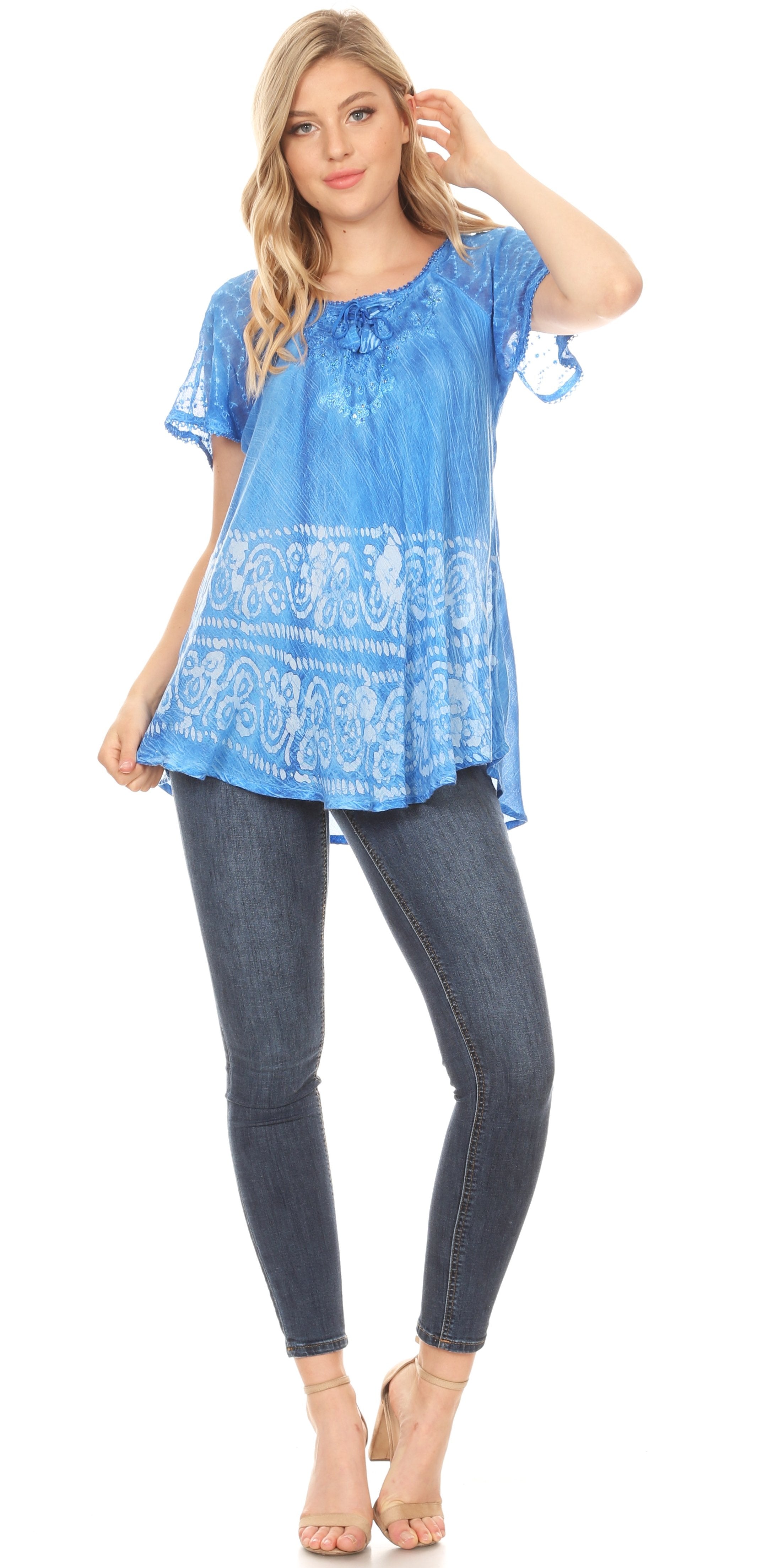 Woman wearing a blue patterned top and dark jeans on a white background