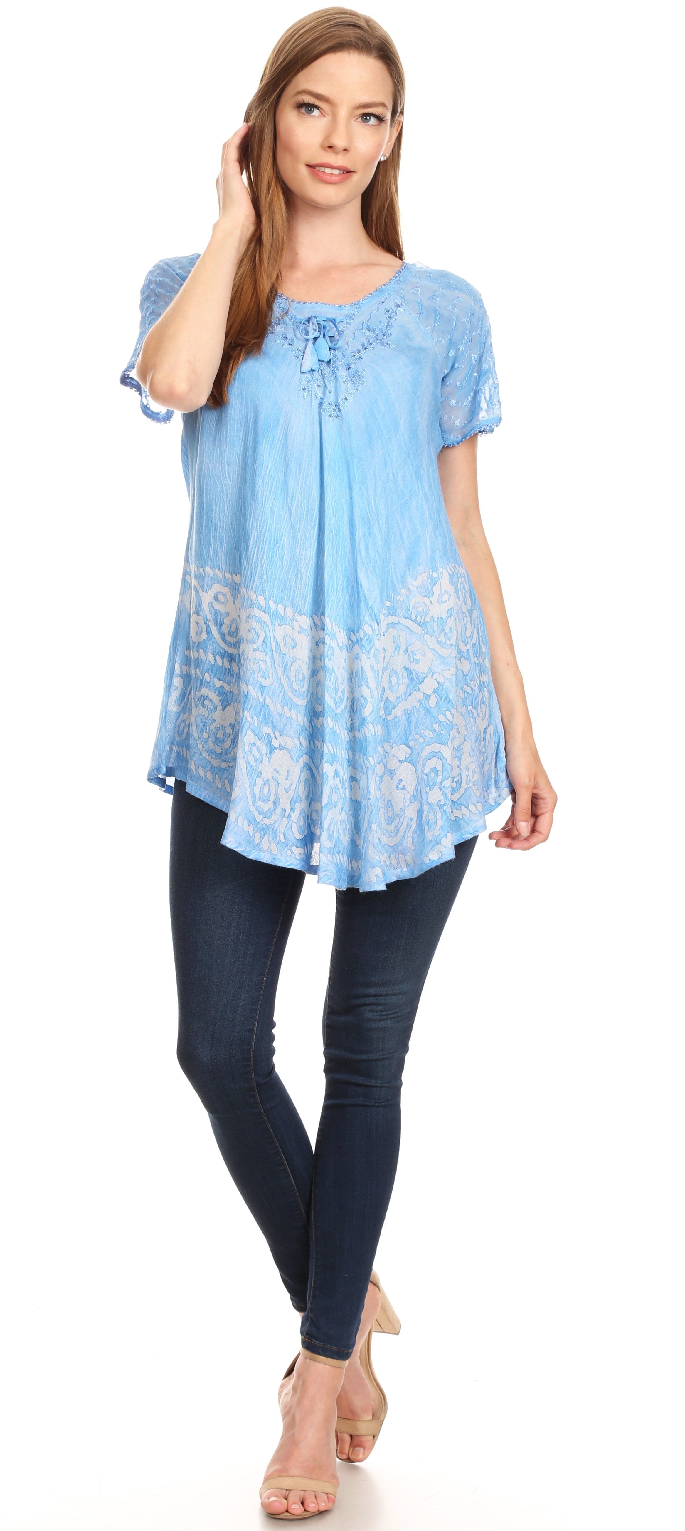 Woman wearing a light blue embroidered tunic with dark jeans on a white background