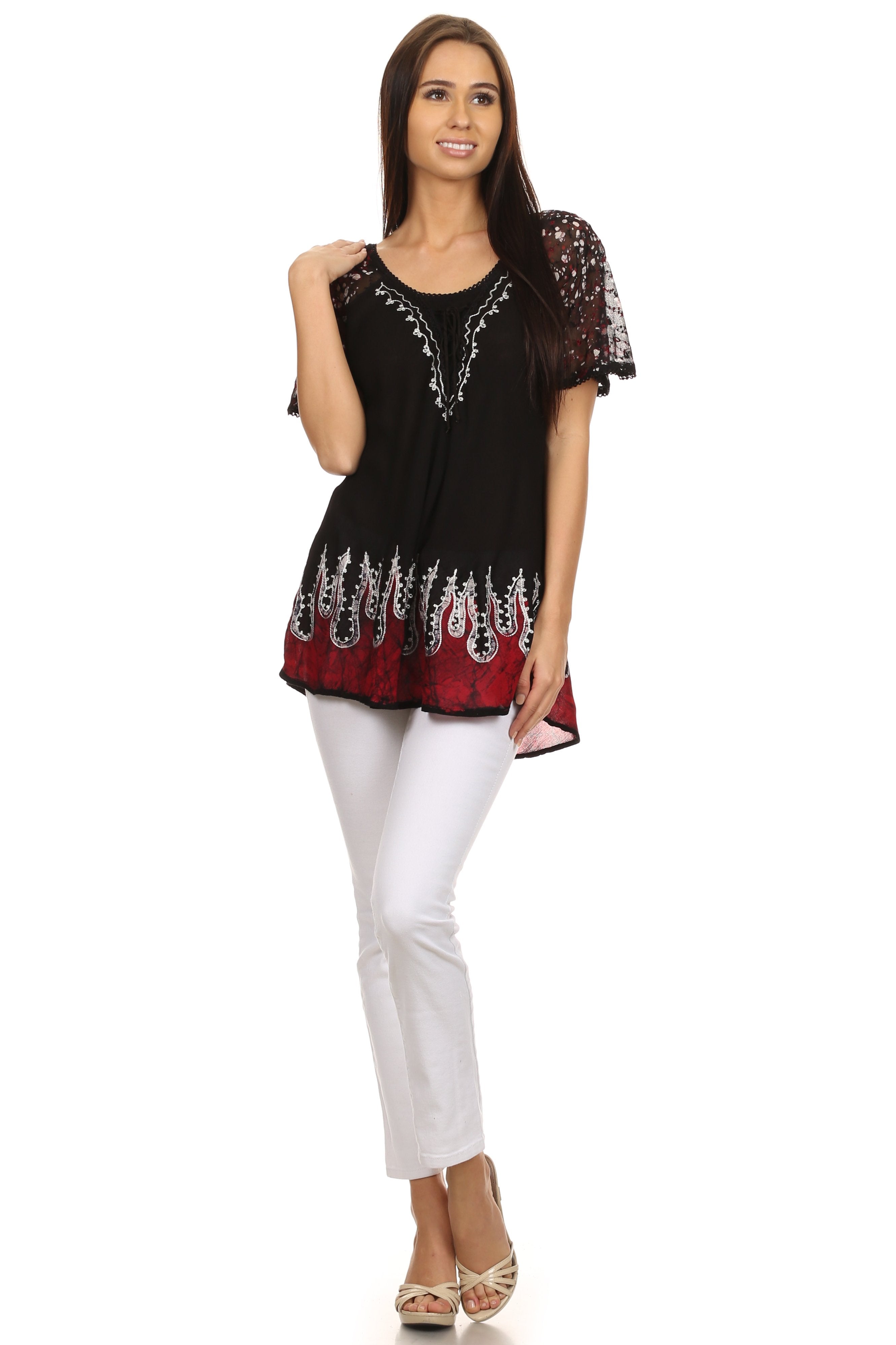 Woman wearing a black and red embroidered top with white pants on a white background