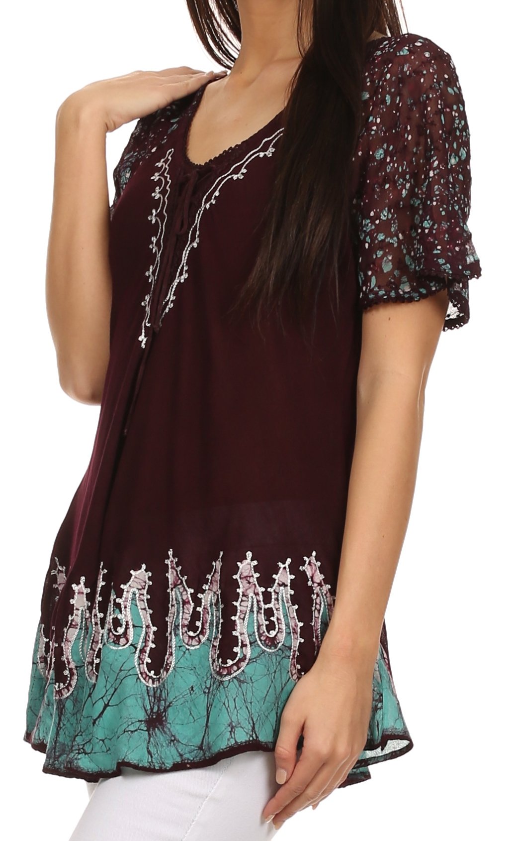 Woman wearing a burgundy and teal patterned top with white pants on a white background
