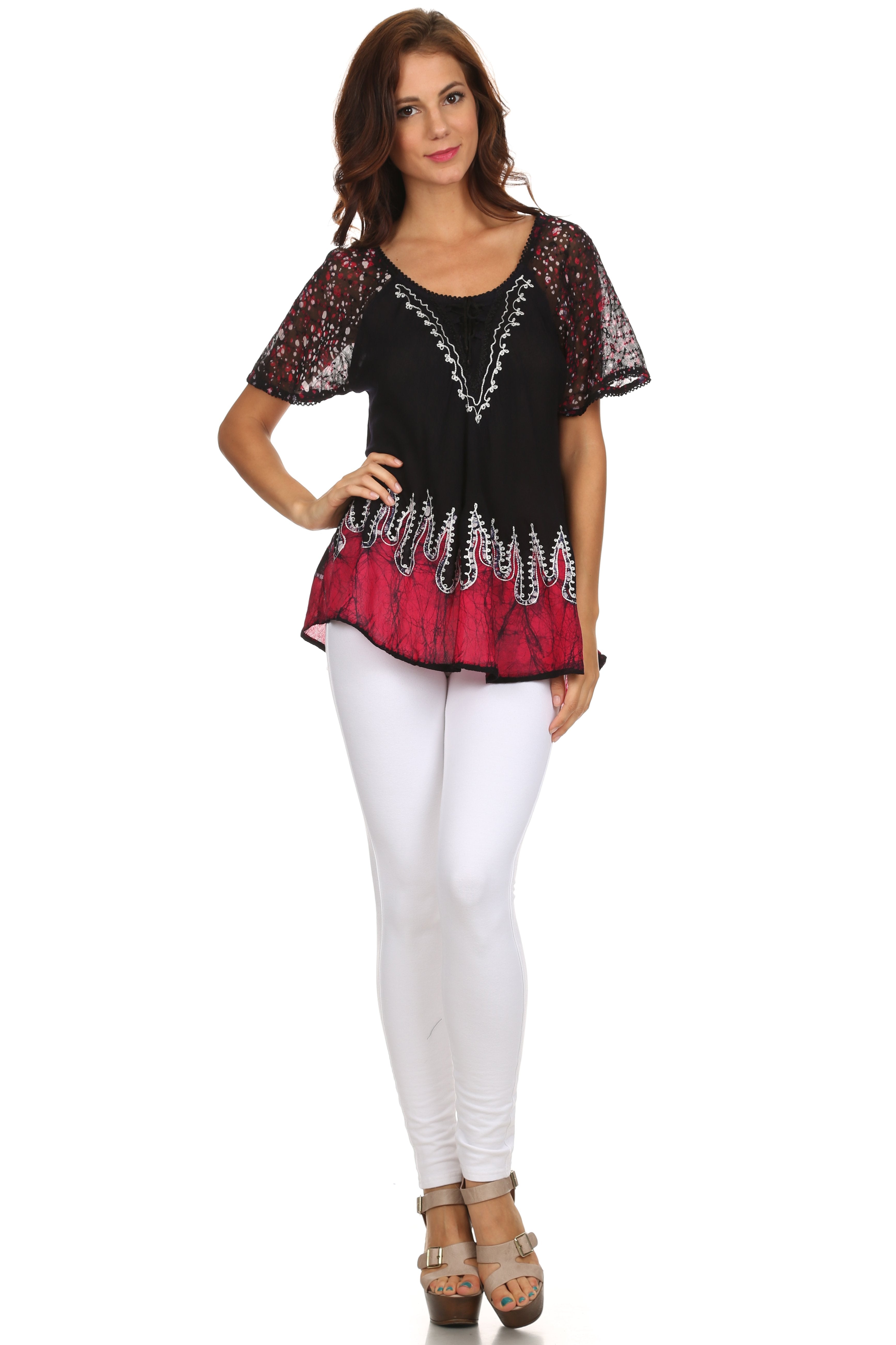 Woman wearing a black and red patterned top with white pants on a white background