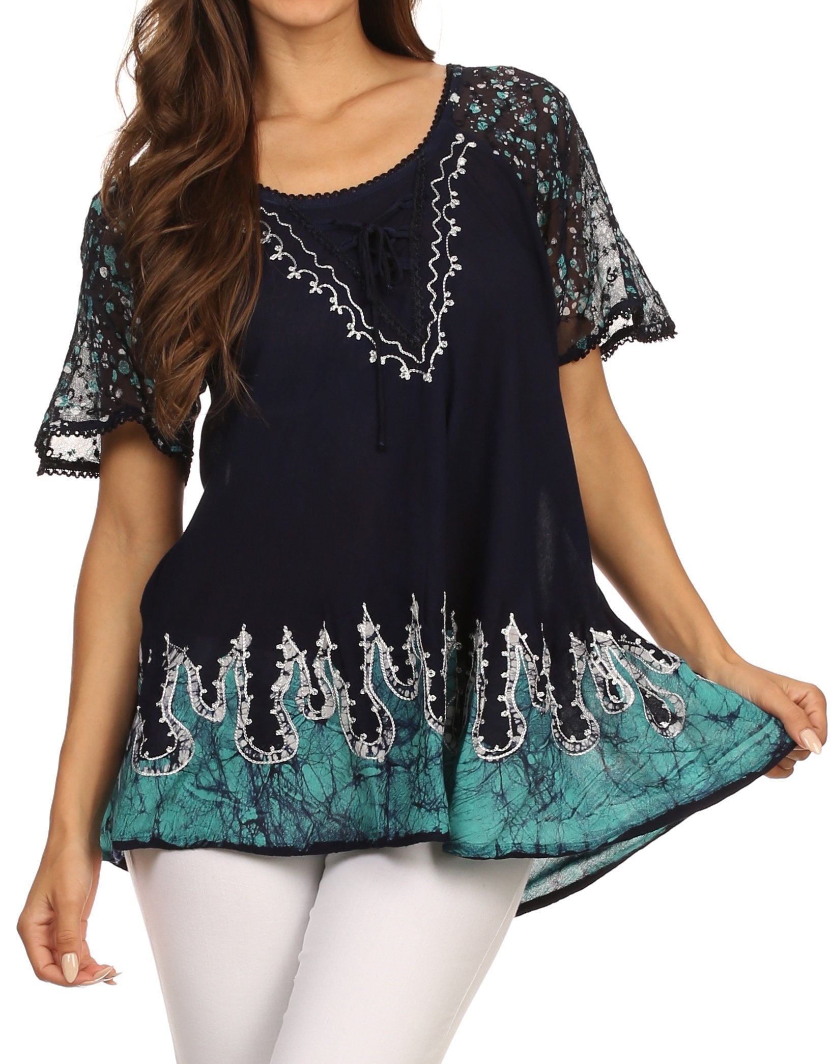 Woman wearing a black and teal embroidered top with white pants on a white background
