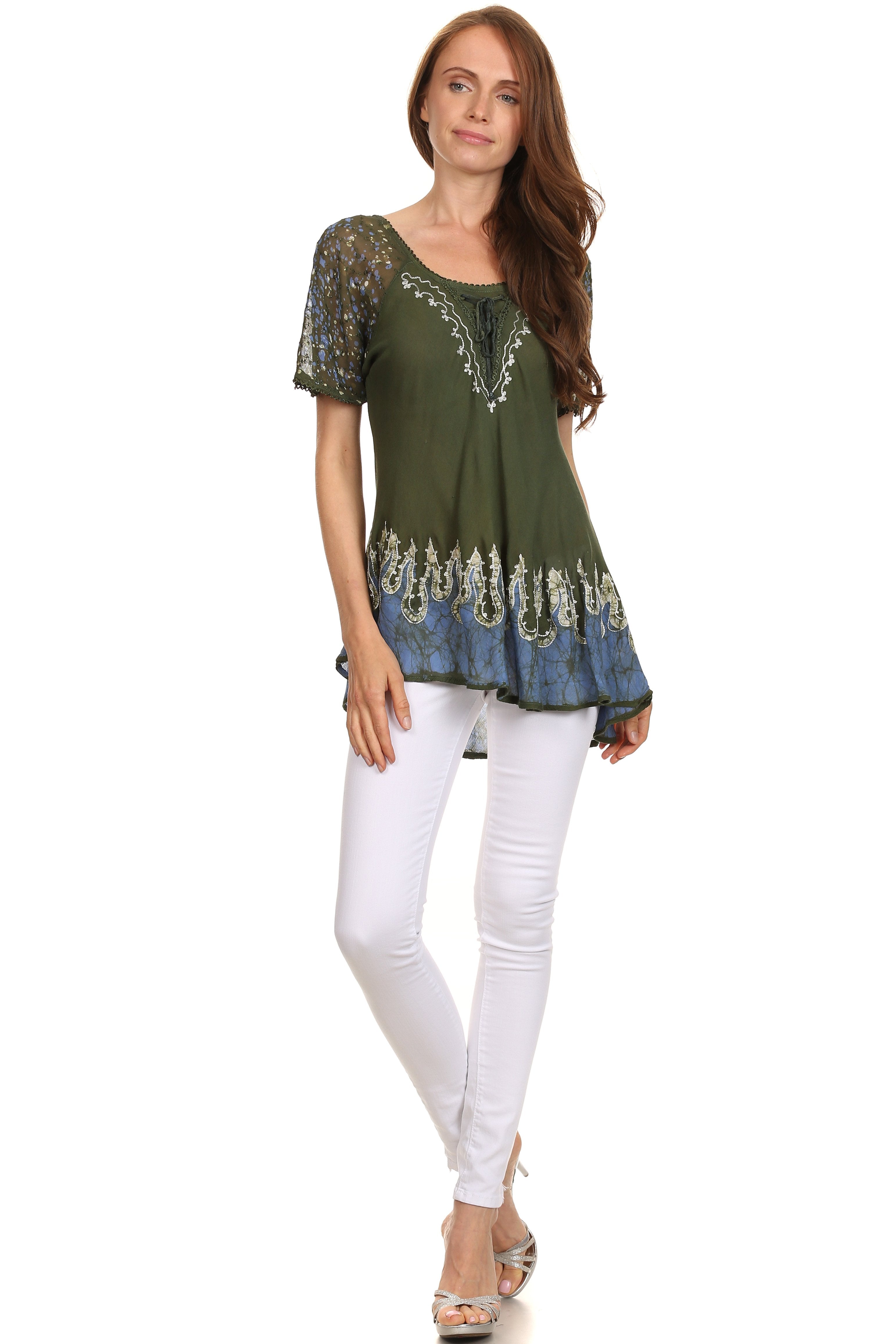 Woman wearing a green embroidered top and white pants on a white background
