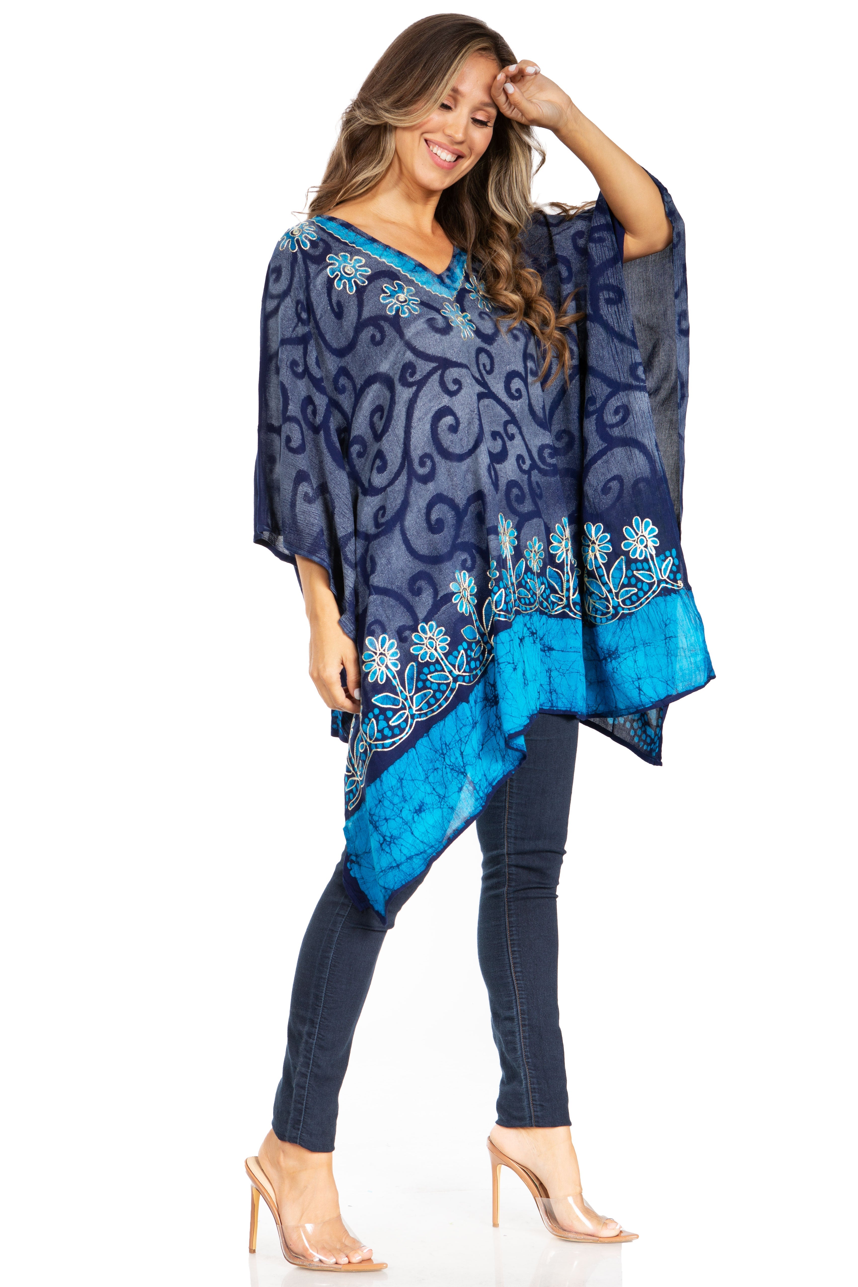 Woman wearing a blue patterned poncho over a blue top and jeans on a white background