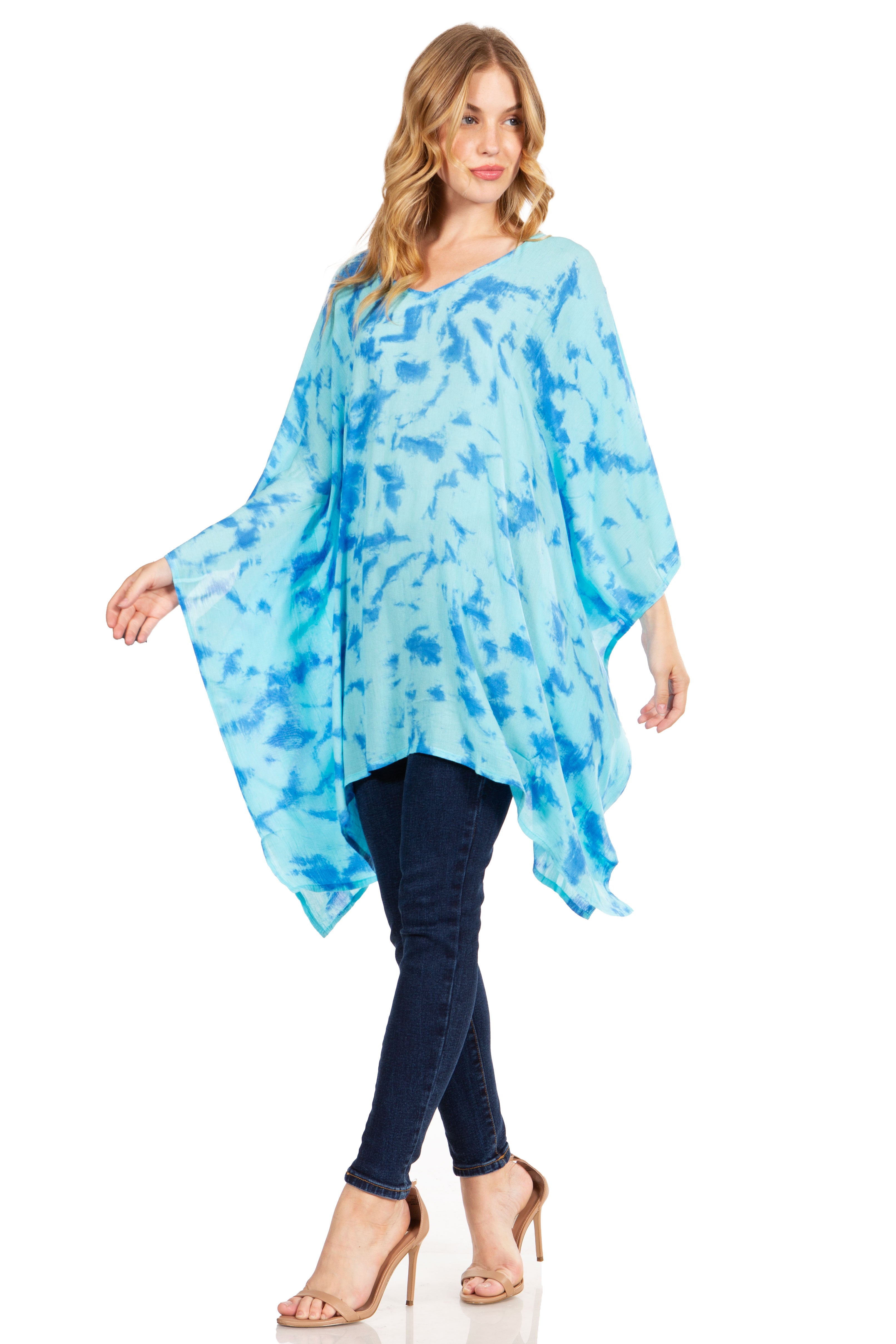 Woman wearing a blue tie-dye poncho over a black top and jeans on a white background