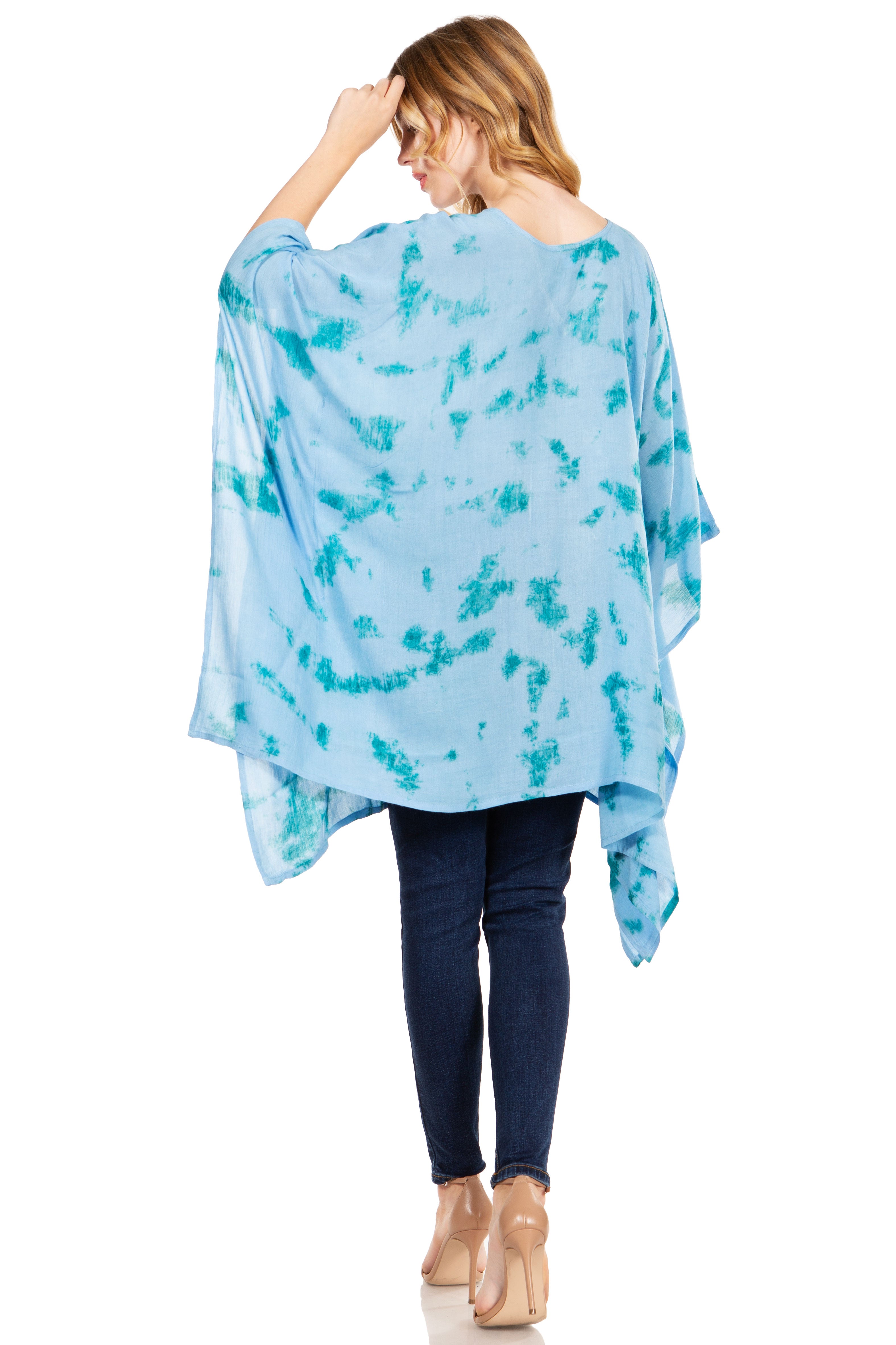 Woman wearing a blue tie-dye poncho over a black top and jeans on a white background