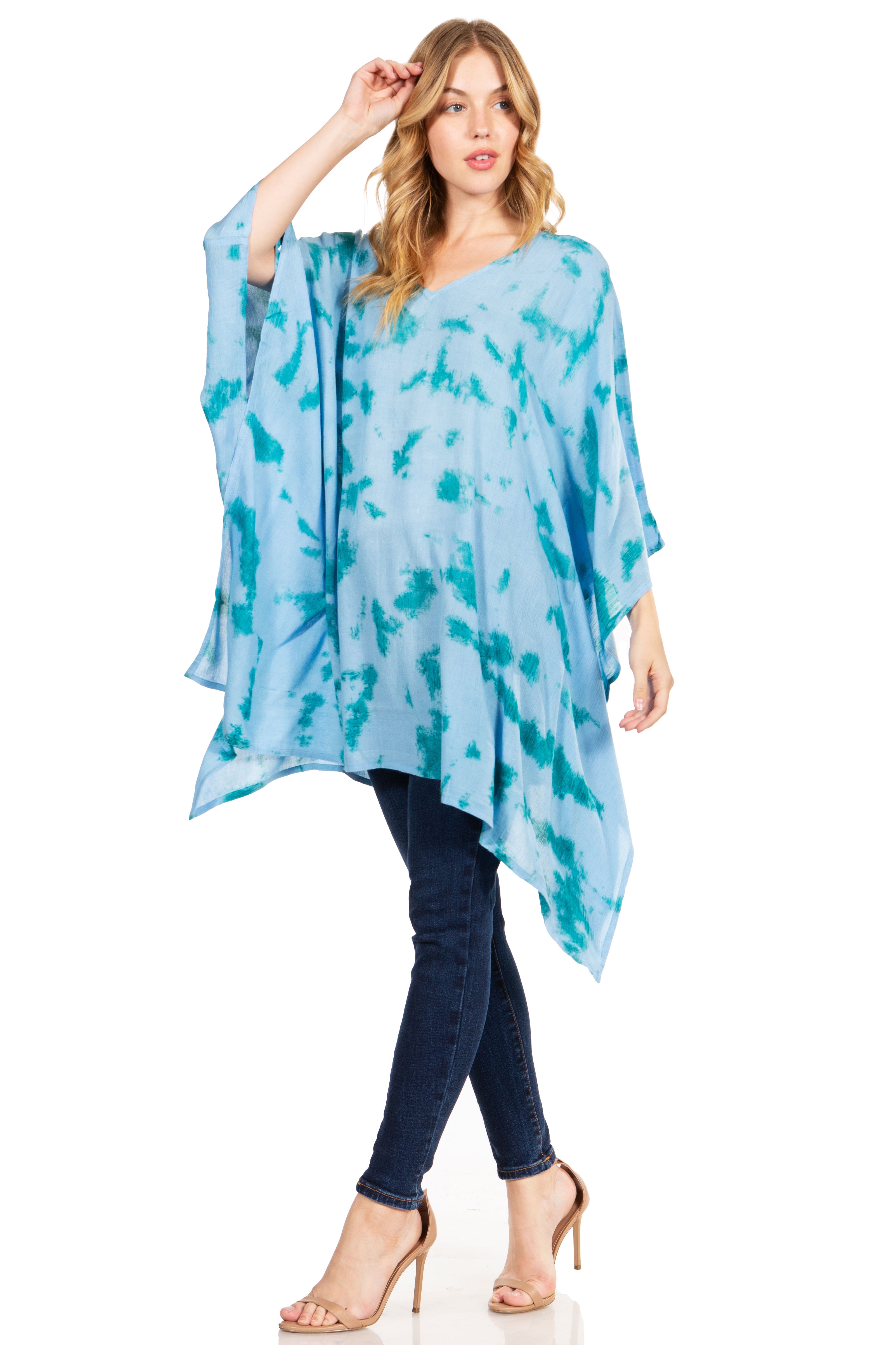 Woman wearing a blue tie-dye poncho over a dark top and jeans on a white background
