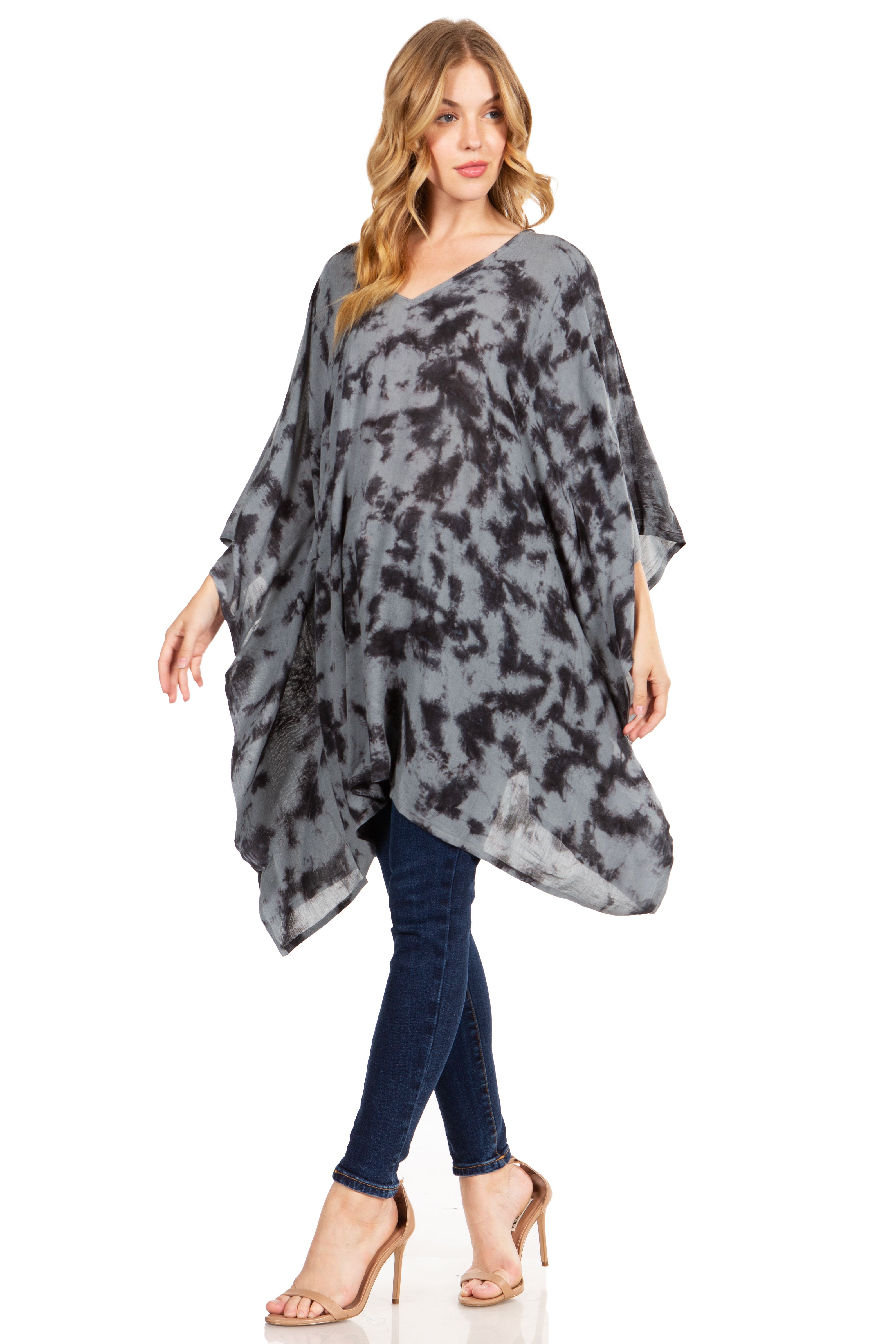 Woman wearing a gray patterned poncho over a blue top and jeans on a white background
