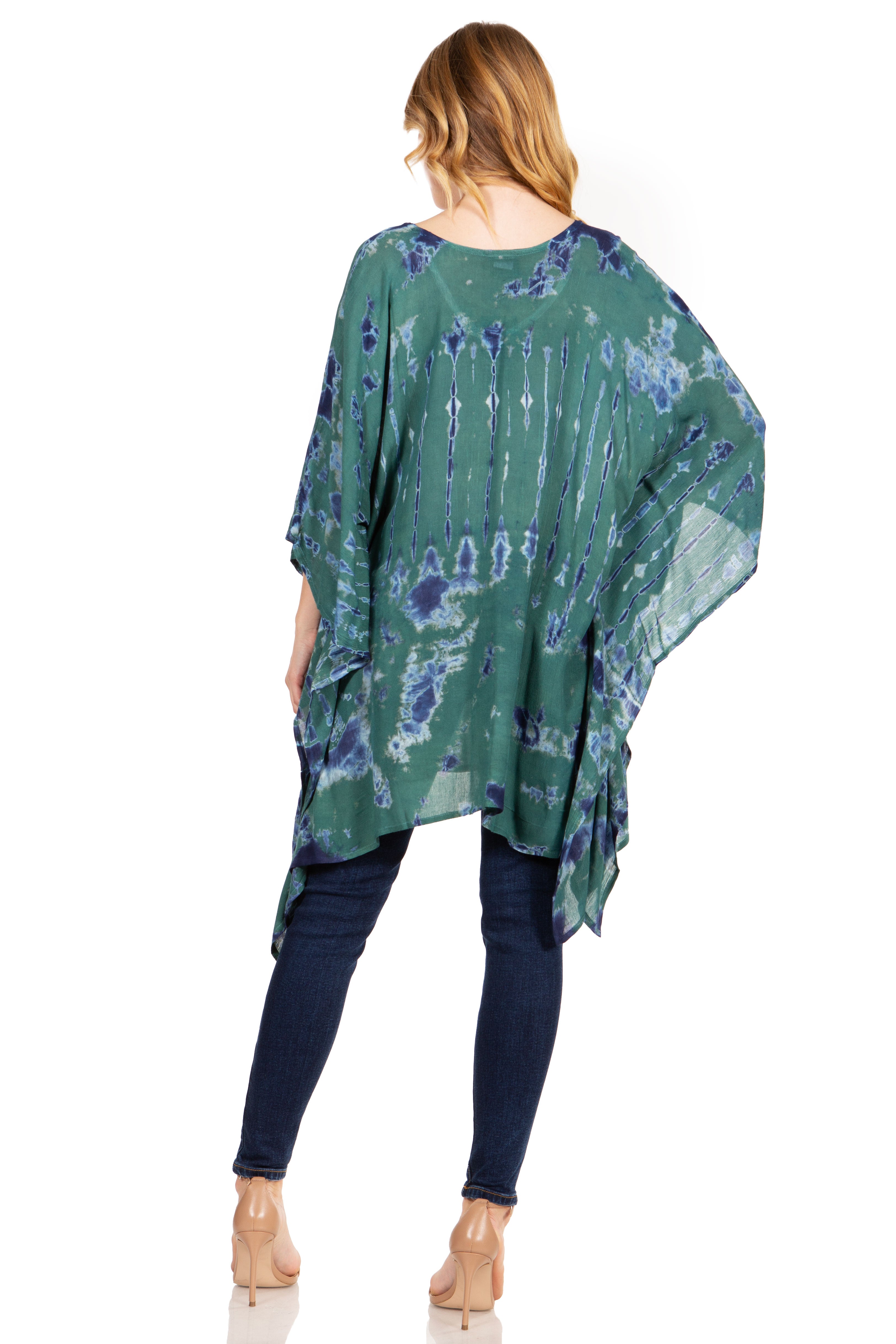 Woman wearing a green and blue patterned poncho over dark pants on a white background