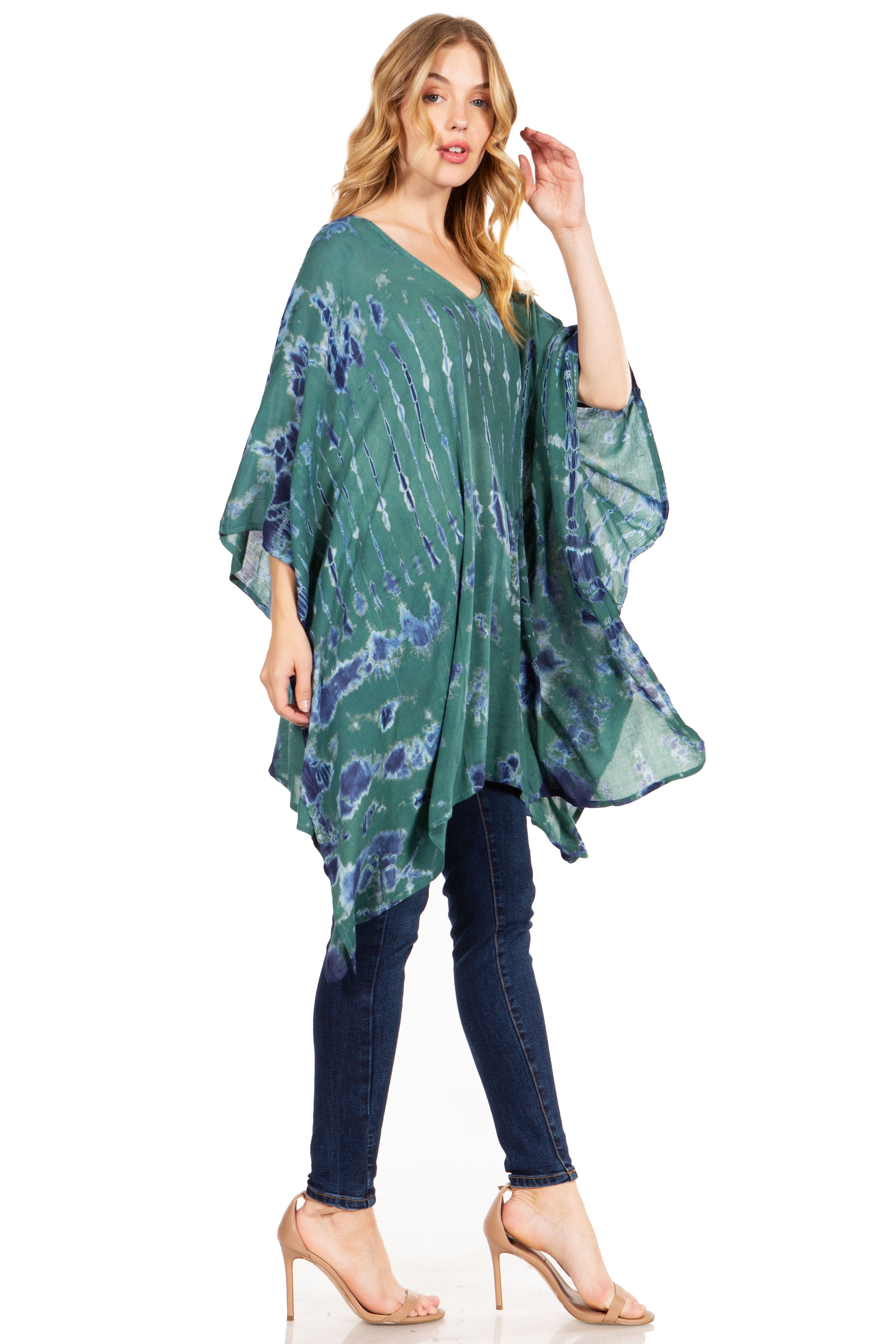 Woman wearing a green and blue patterned poncho over a dark blue top and jeans on a white background