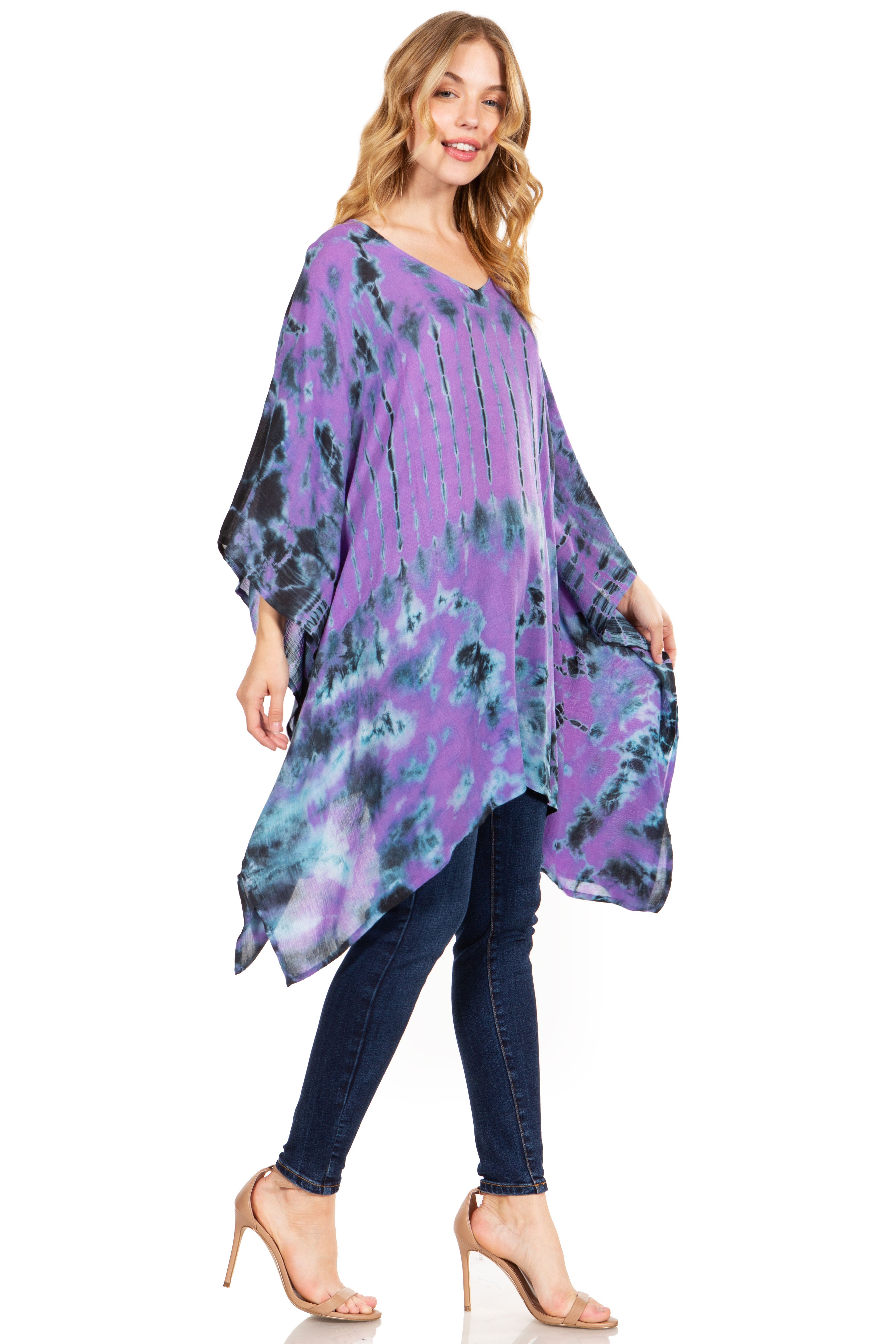 Woman wearing a purple tie-dye poncho over a black top and blue jeans on a white background