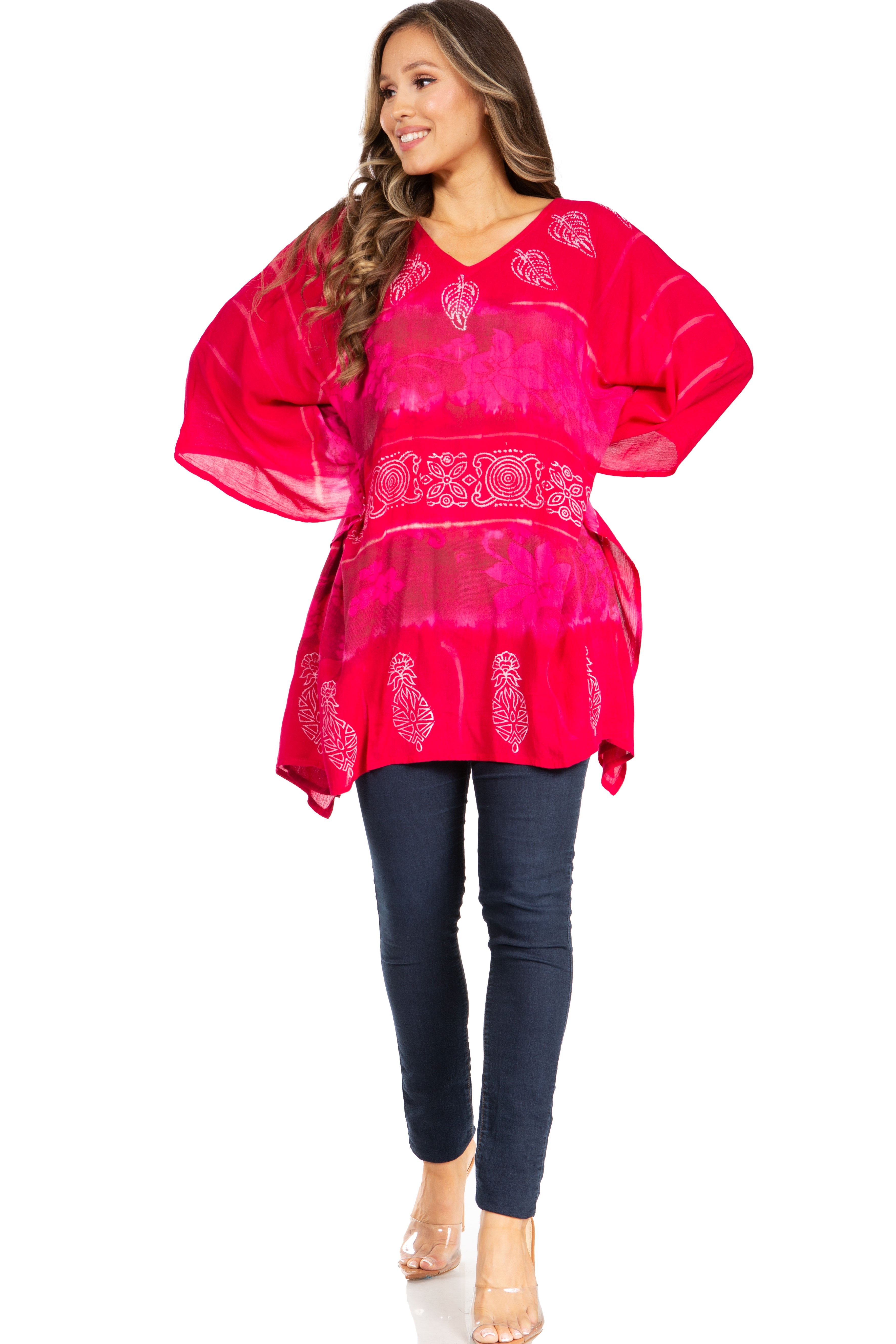 Woman wearing a bright pink embroidered top and dark blue pants on a white background