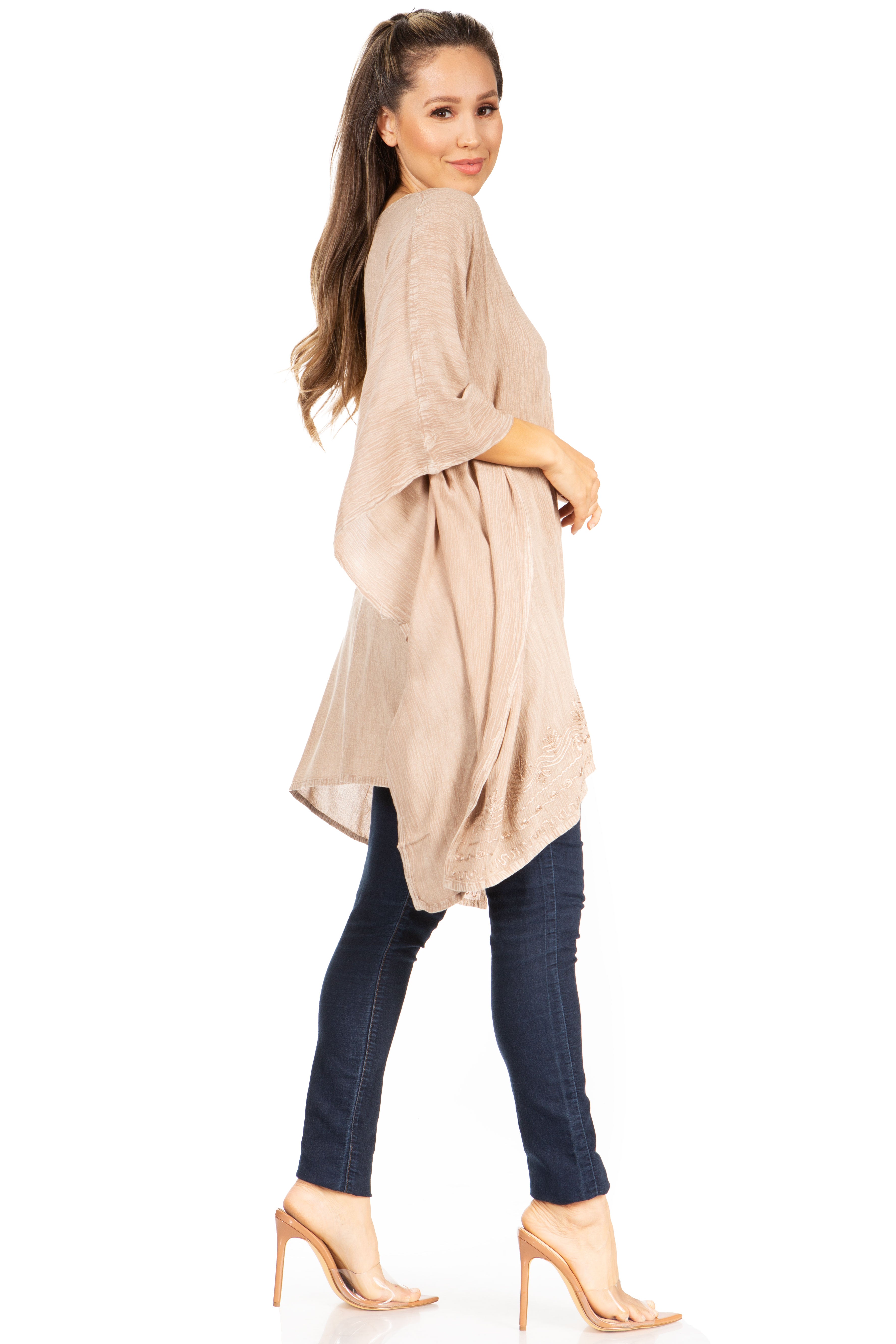 Woman wearing a beige long top and dark jeans on a white background