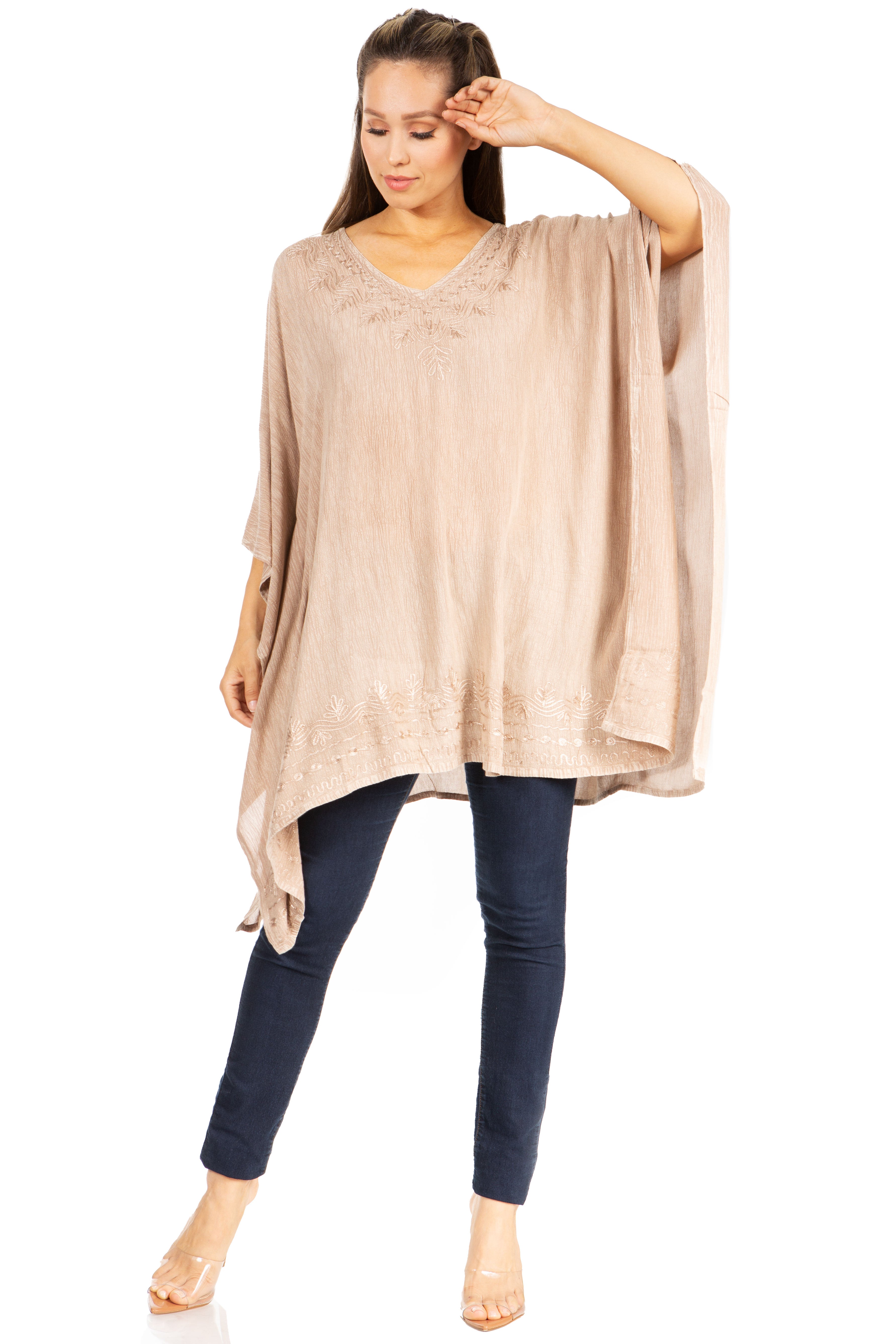 Woman wearing a beige poncho and dark blue pants on a white background