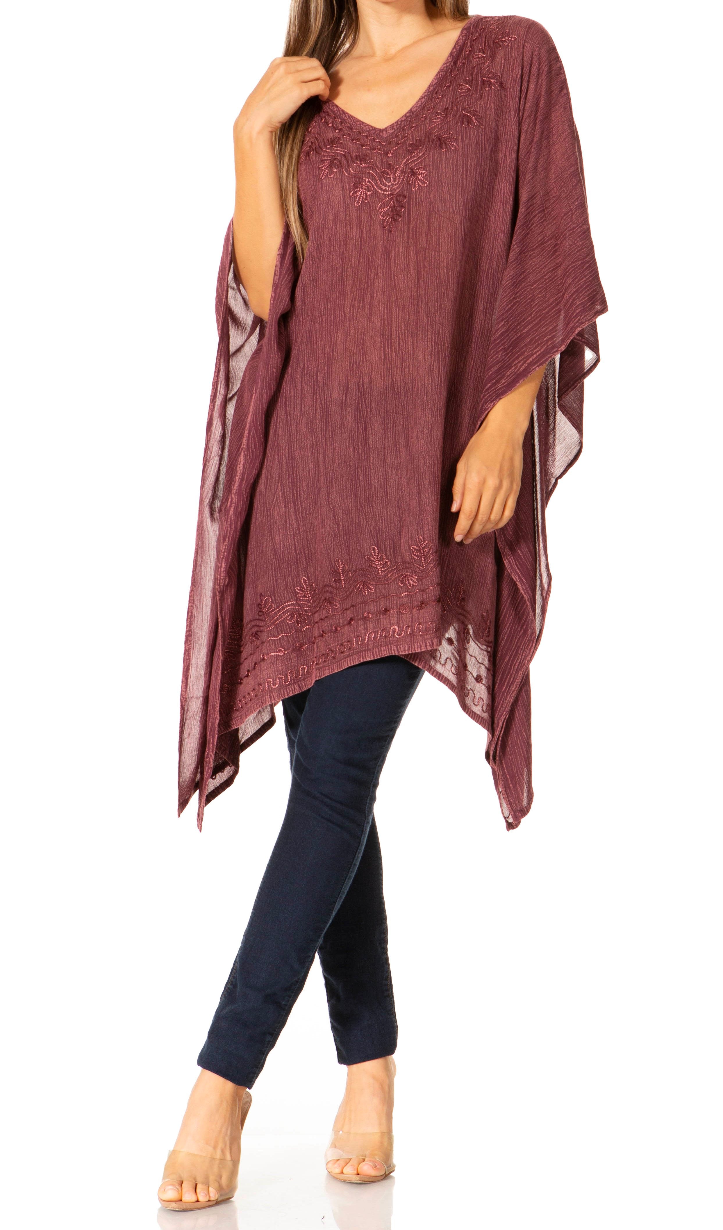 Woman wearing a burgundy poncho over a blue top and pants on a white background