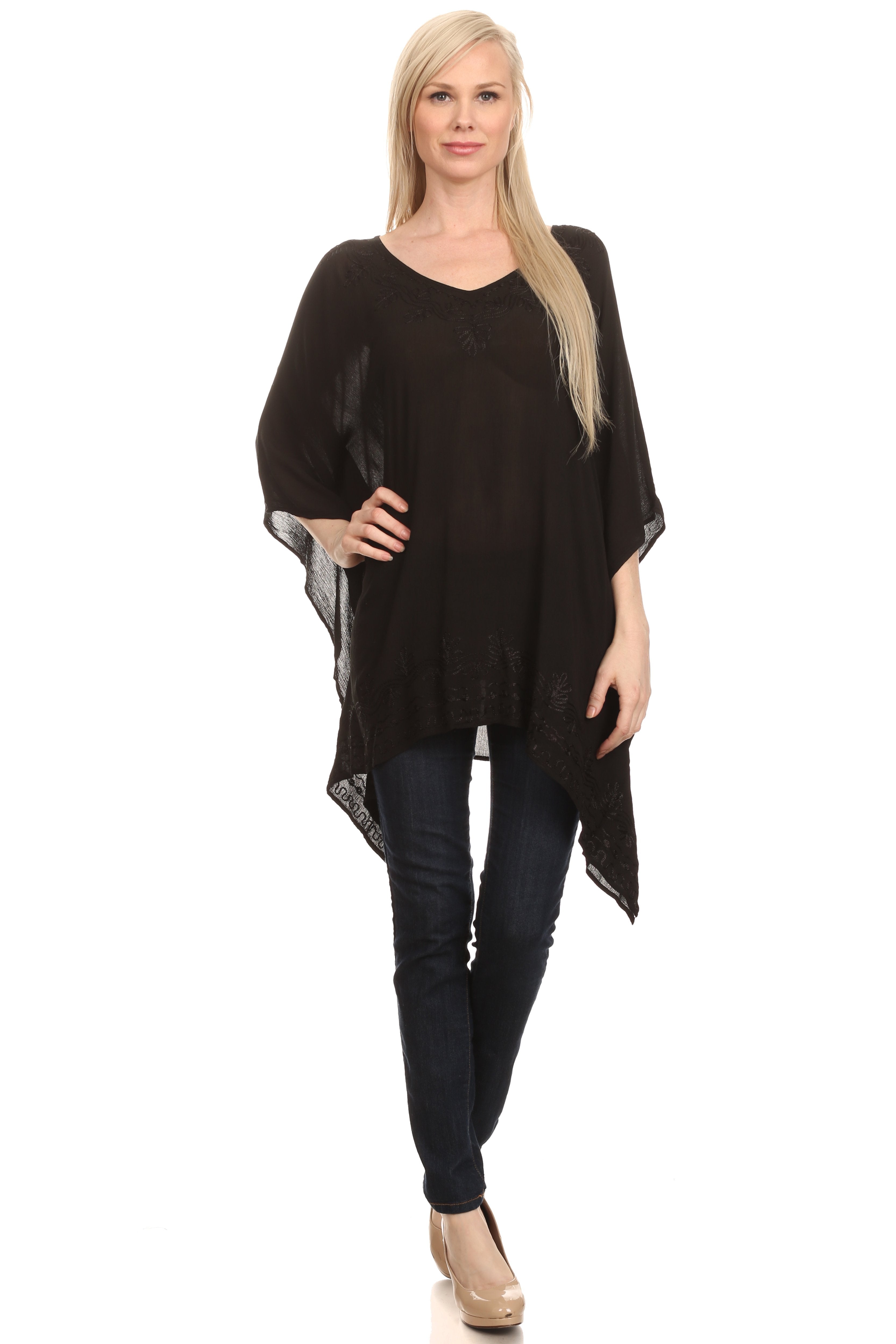 Woman wearing a black poncho over a black top and jeans on a white background