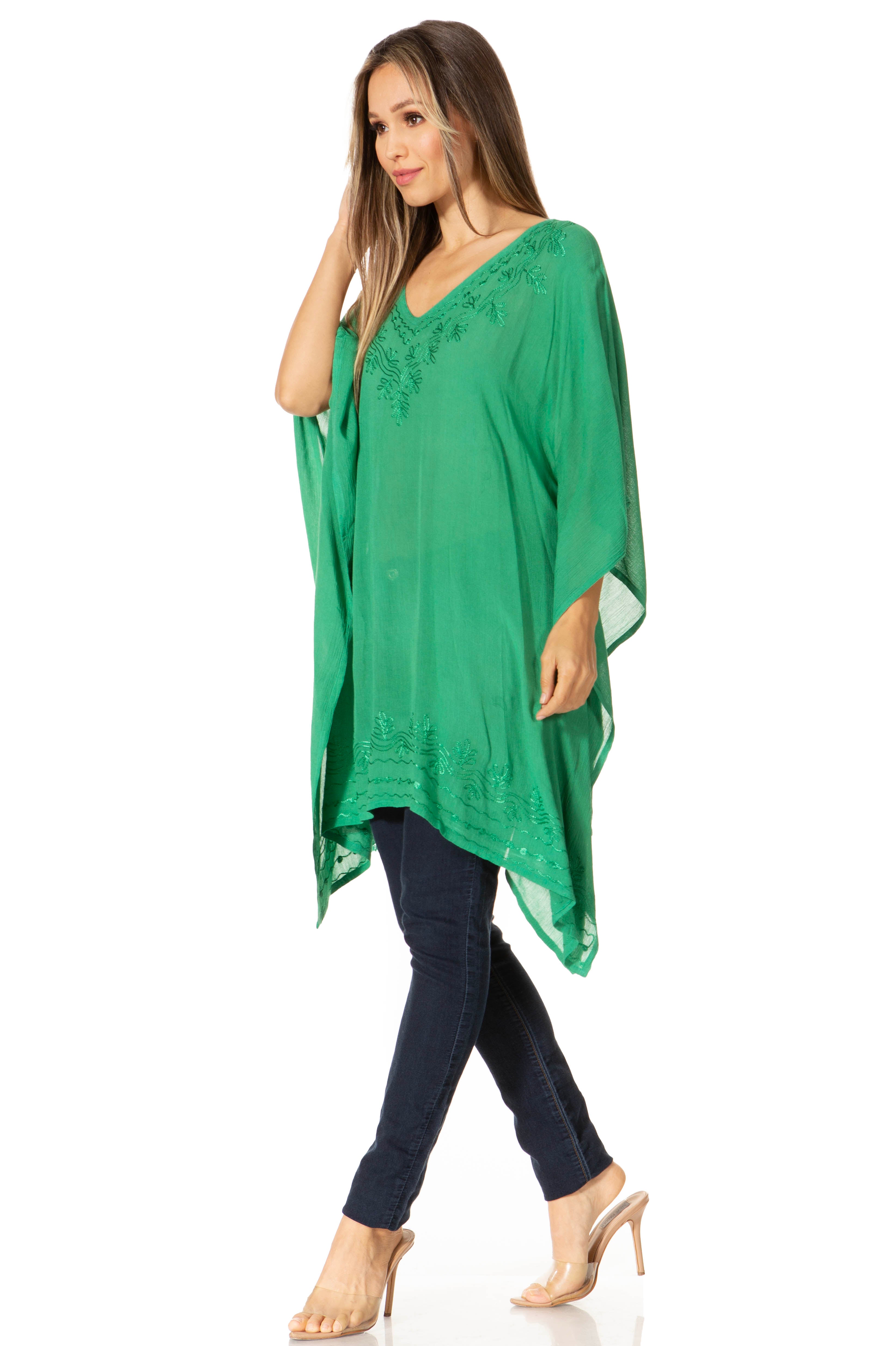 Woman wearing a green poncho over a black top and jeans on a white background