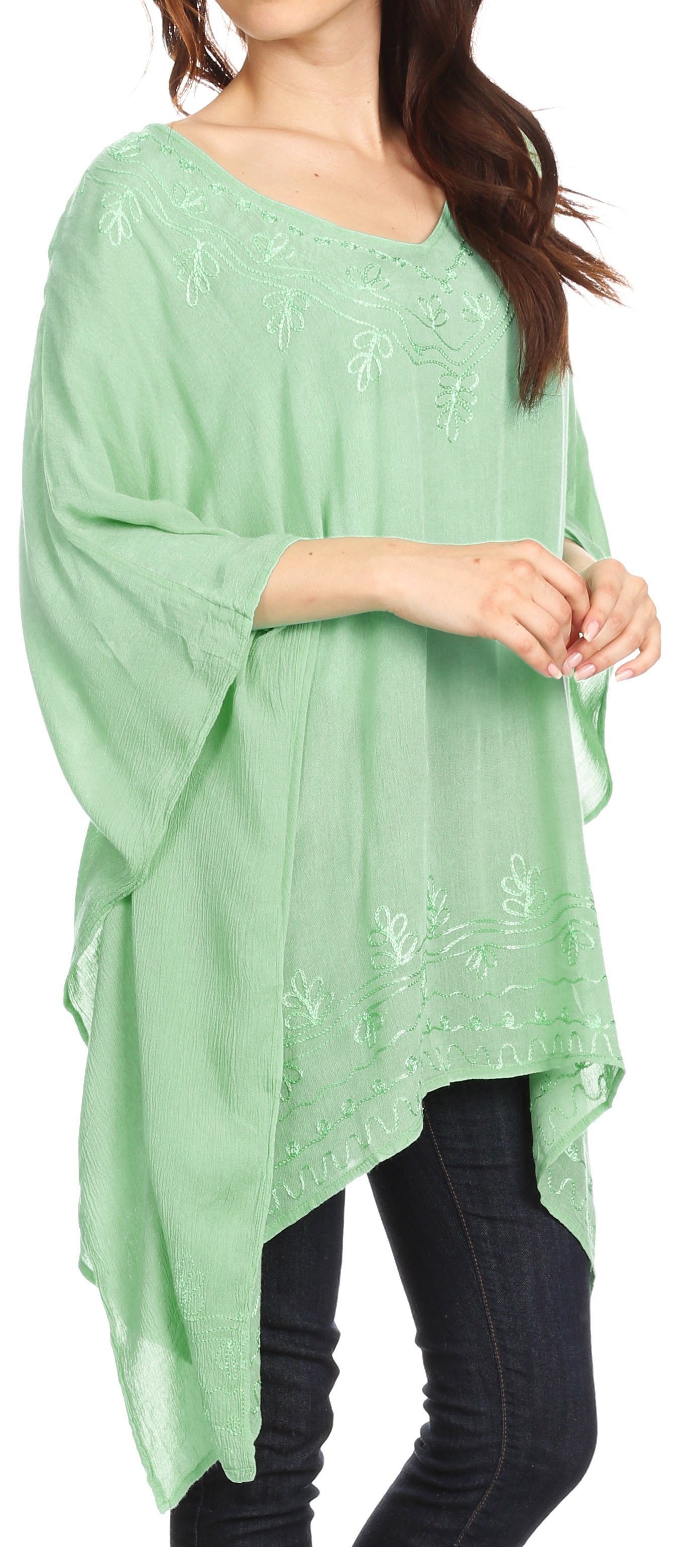 Woman wearing a light green poncho with floral embroidery, standing against a neutral background.