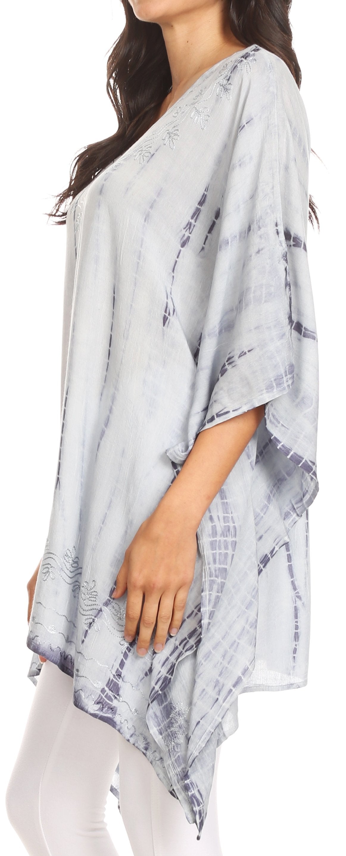 Woman wearing a light blue and white patterned poncho with white pants.