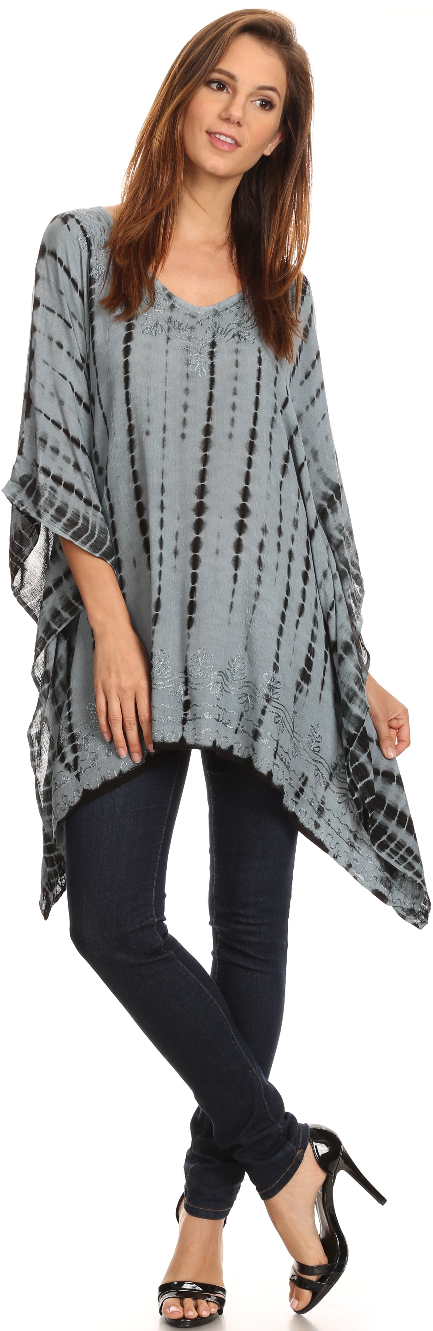 Woman wearing a gray tie-dye poncho over a blue top and black pants on a white background