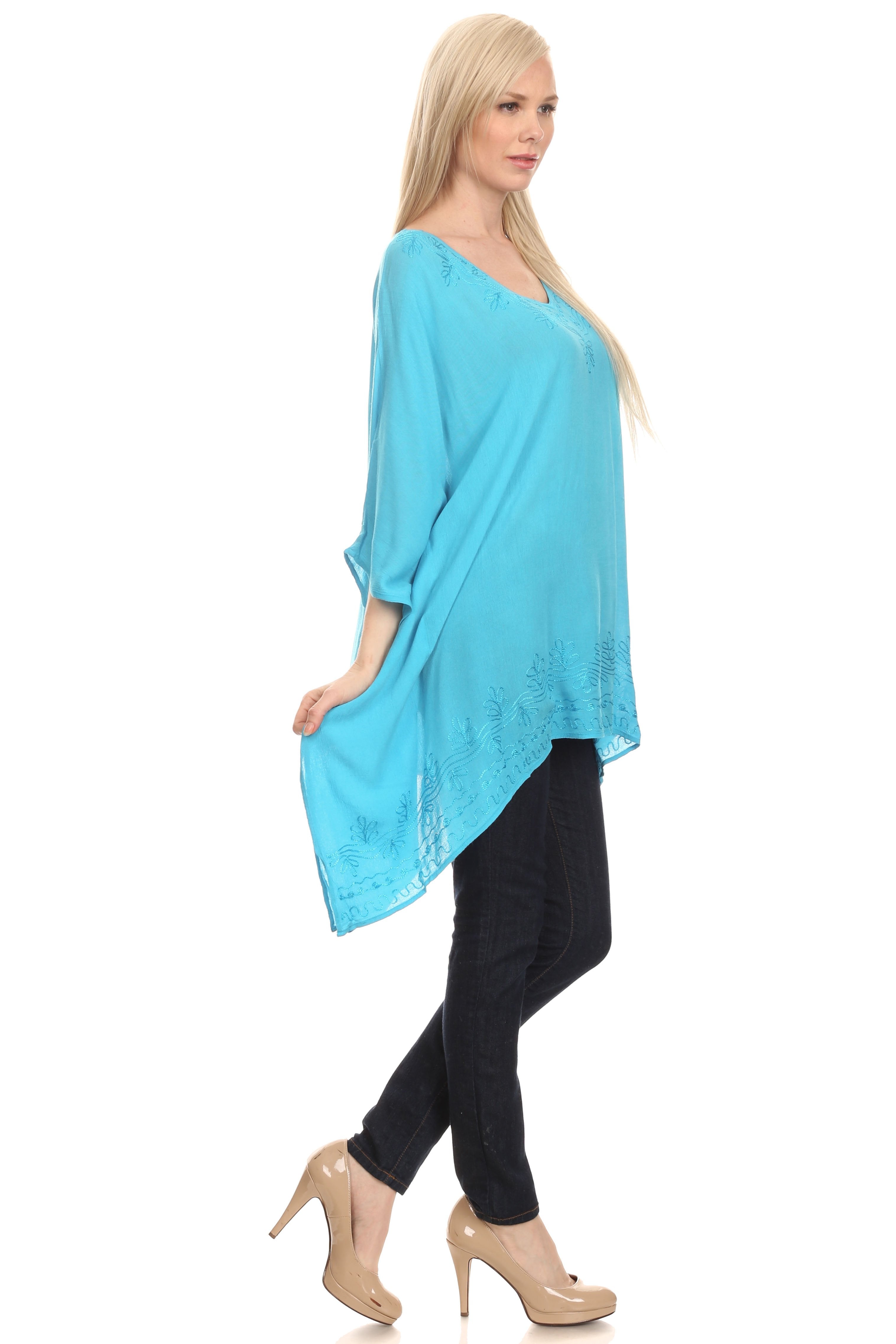 Woman wearing a turquoise poncho over a black outfit on a white background