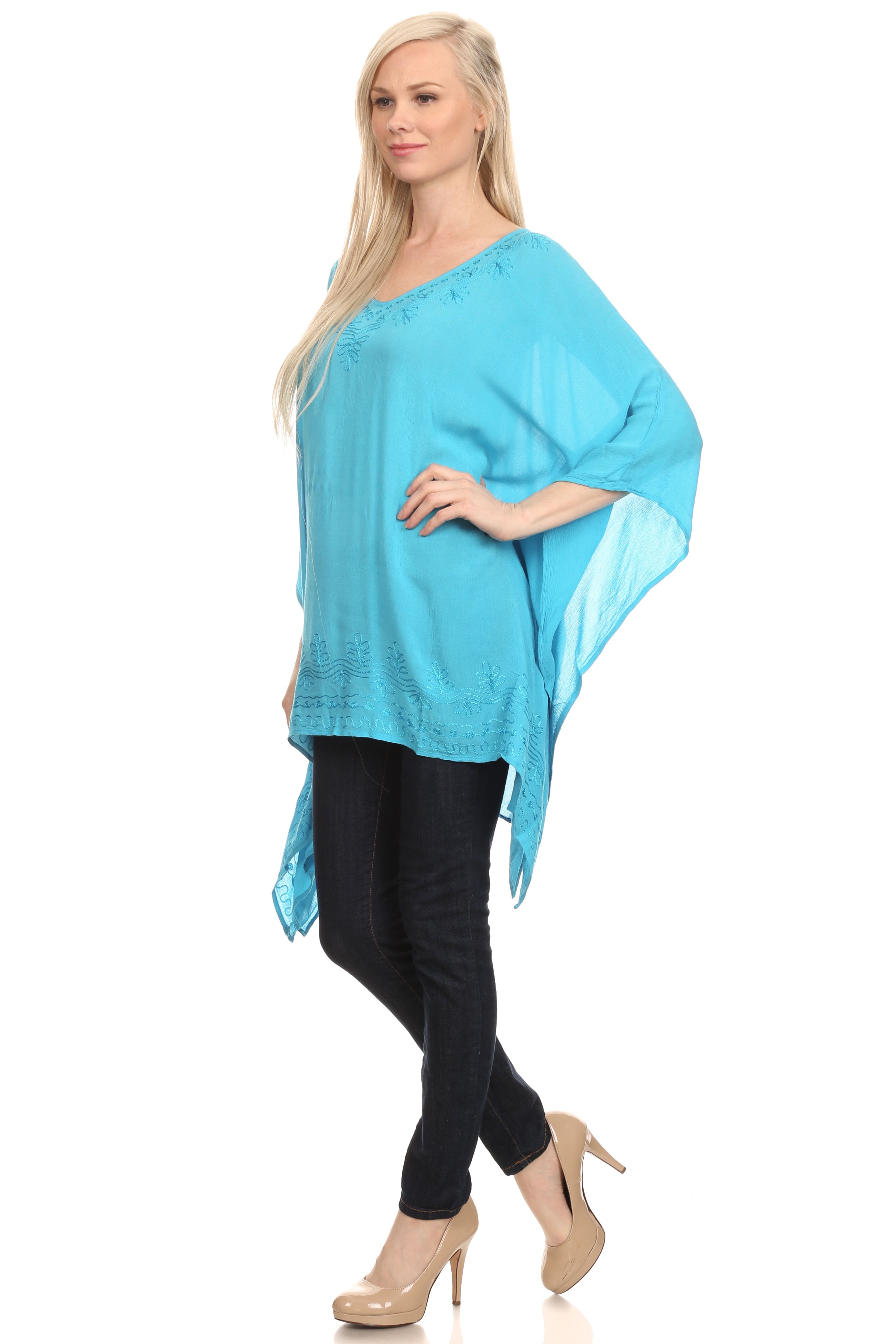 Woman wearing a turquoise poncho over a black outfit on a white background