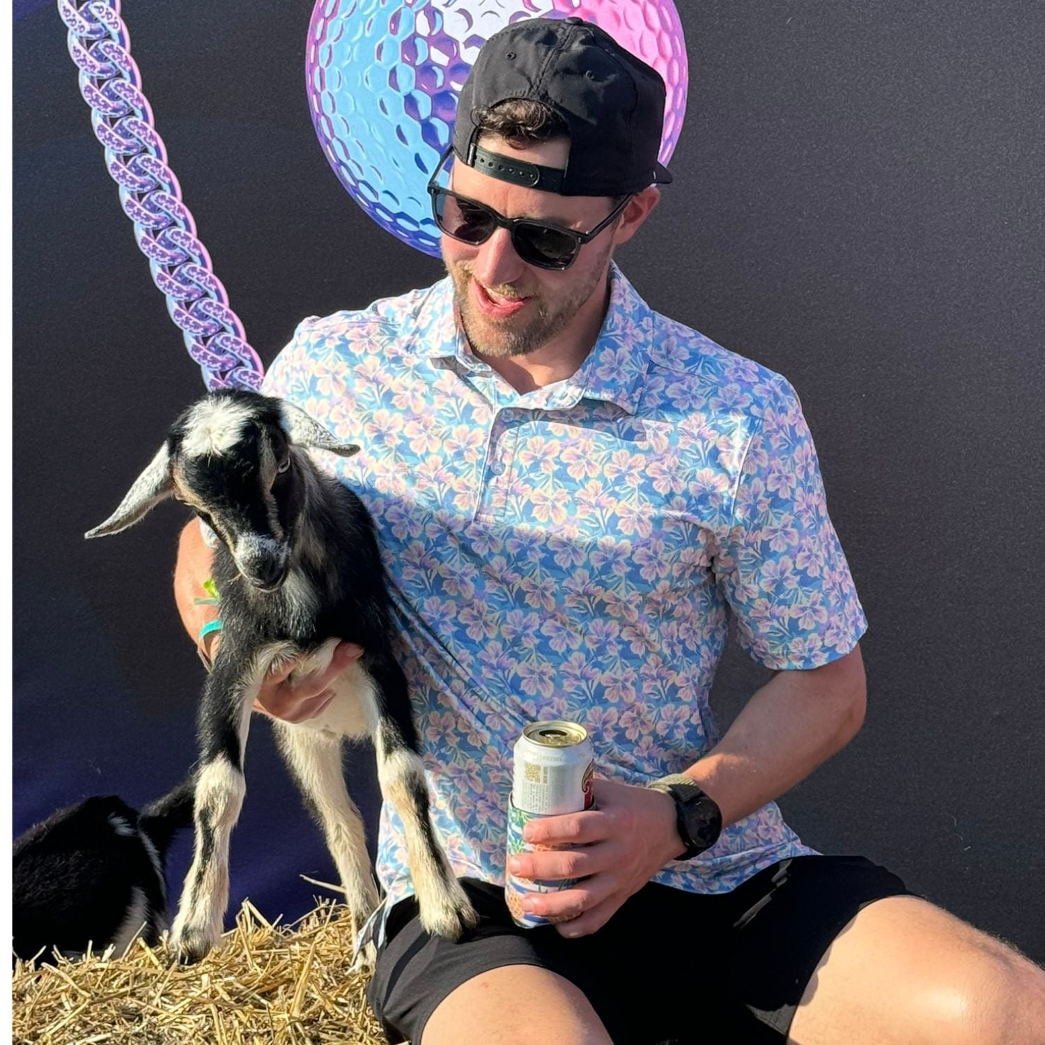 Man holding a goat and a can, with colorful balls in the background