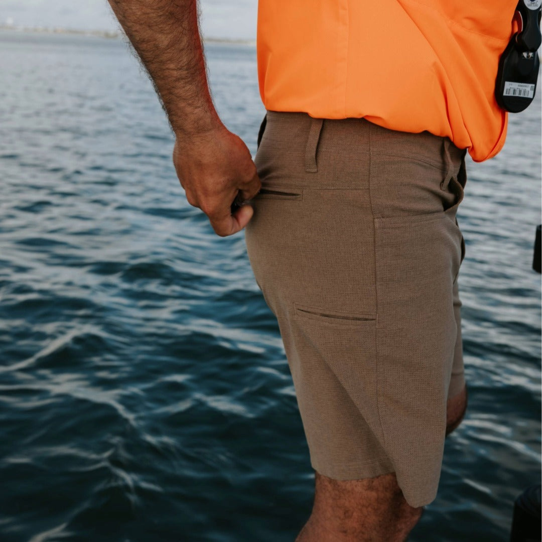 Person wearing brown shorts and an orange jacket by a body of water