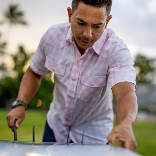 Man in a pink shirt using a grill outdoors