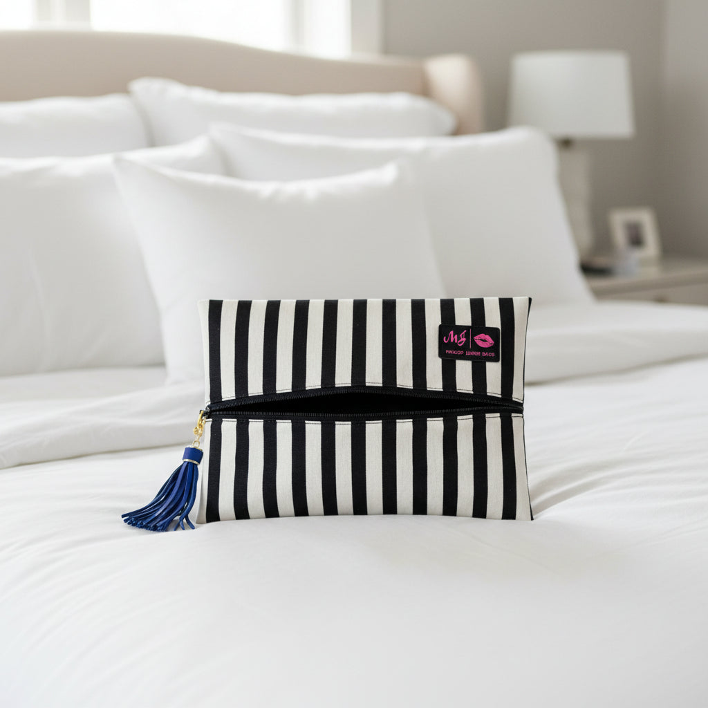 Black and white striped makeup bag with a blue tassel on a light gray background