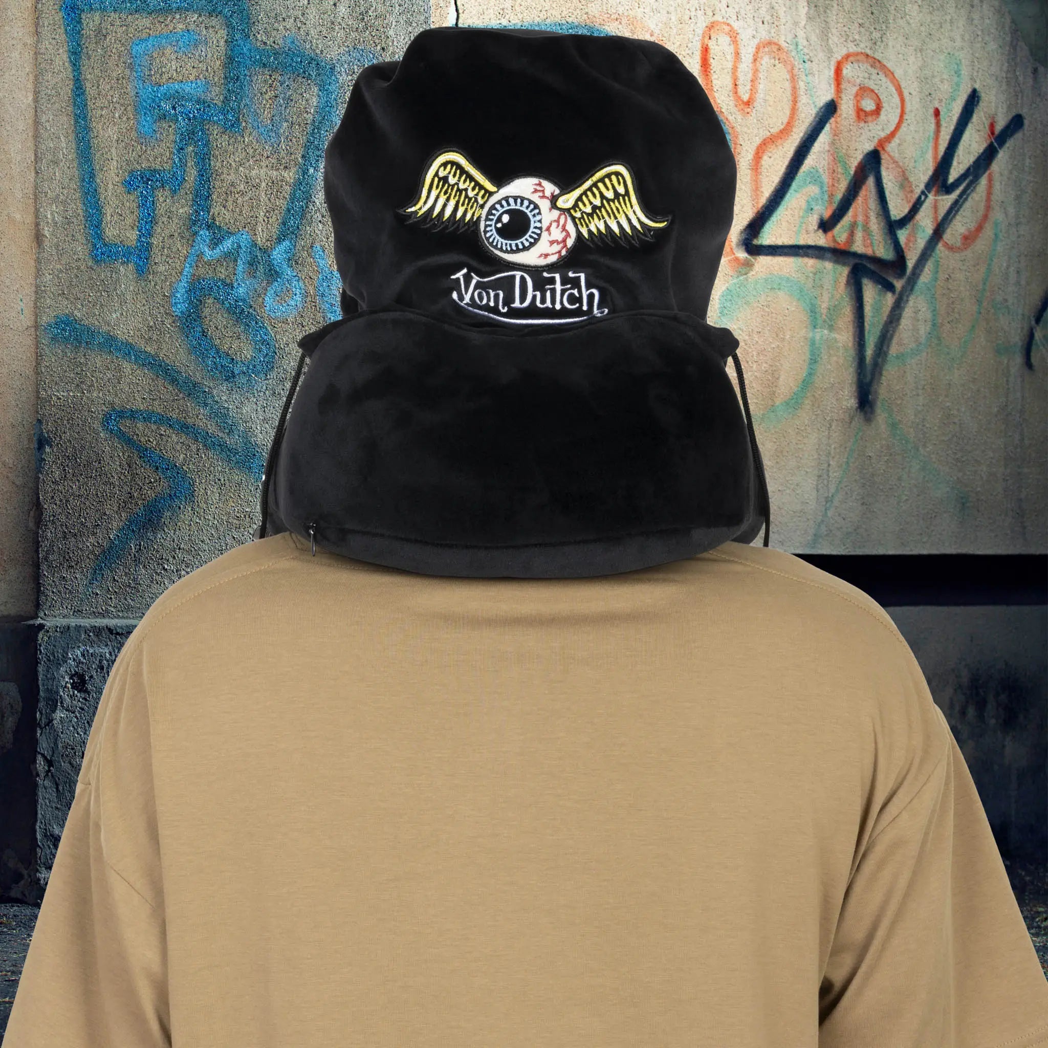 Person wearing a black hoodie with 'Von Dutch' logo against a graffiti-covered wall.