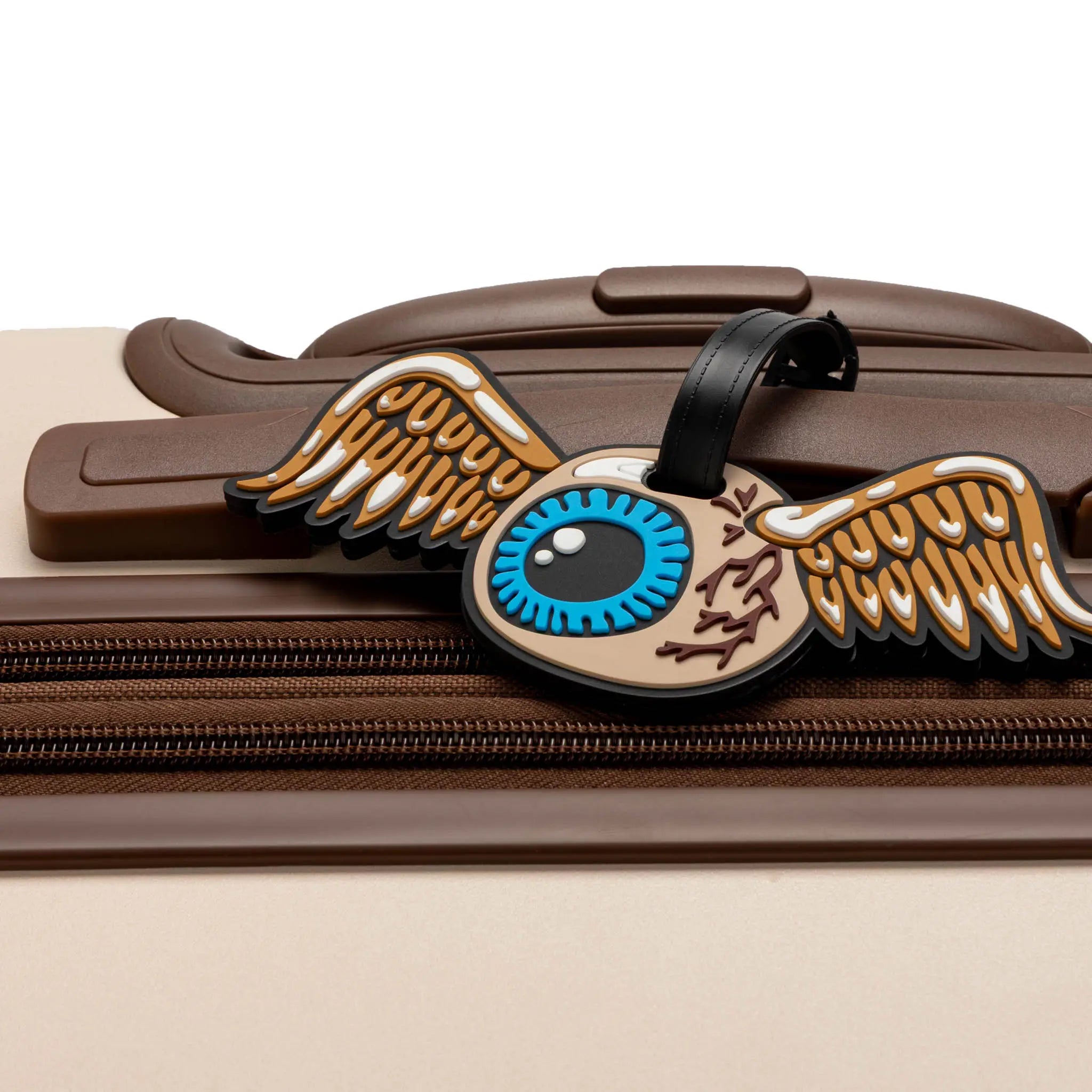 Decorative luggage tag with wings and an eye design on a suitcase.