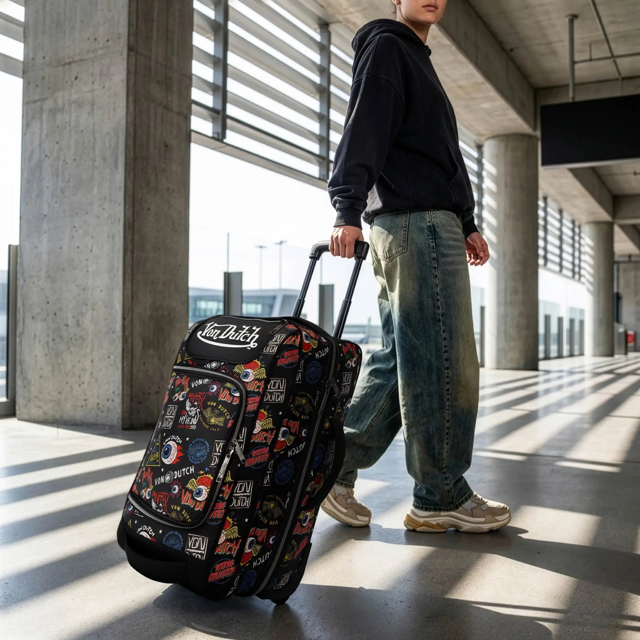 Person pulling a suitcase with multiple stickers in an airport terminal