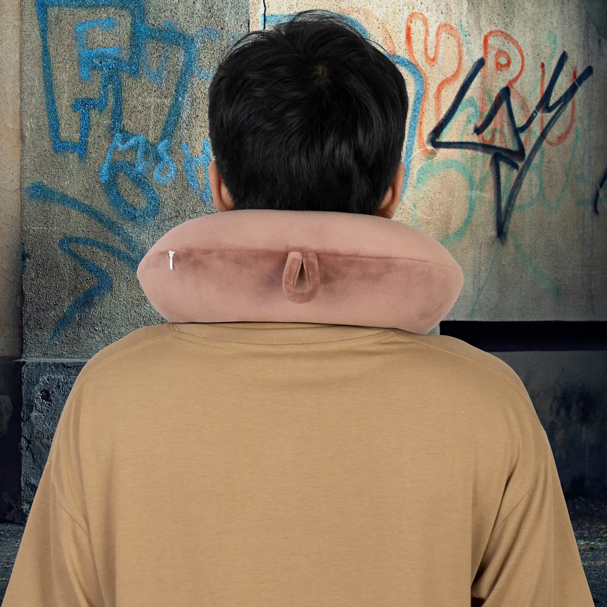 Person wearing a neck pillow with graffiti on the wall