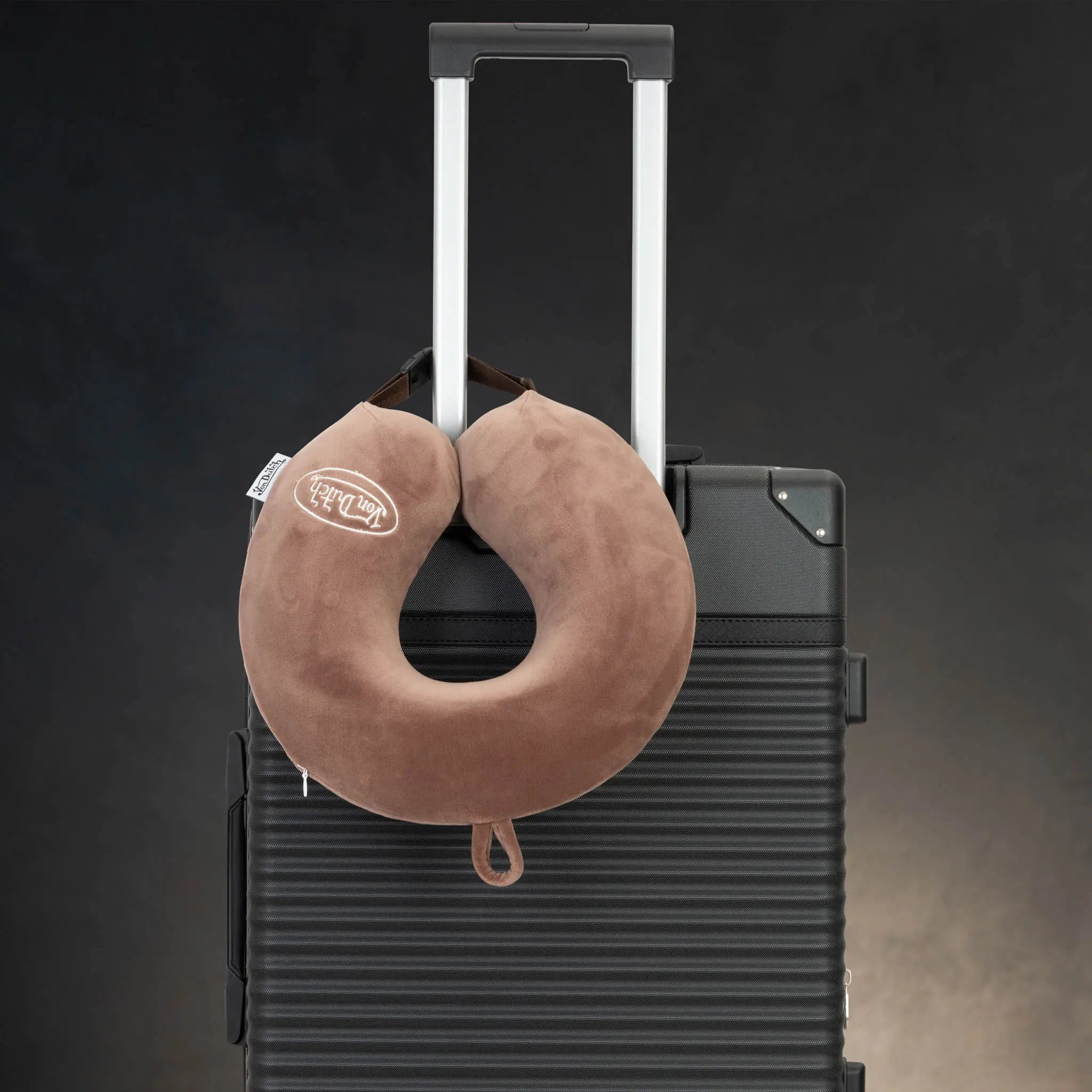 Brown travel neck pillow on a black suitcase with a dark background