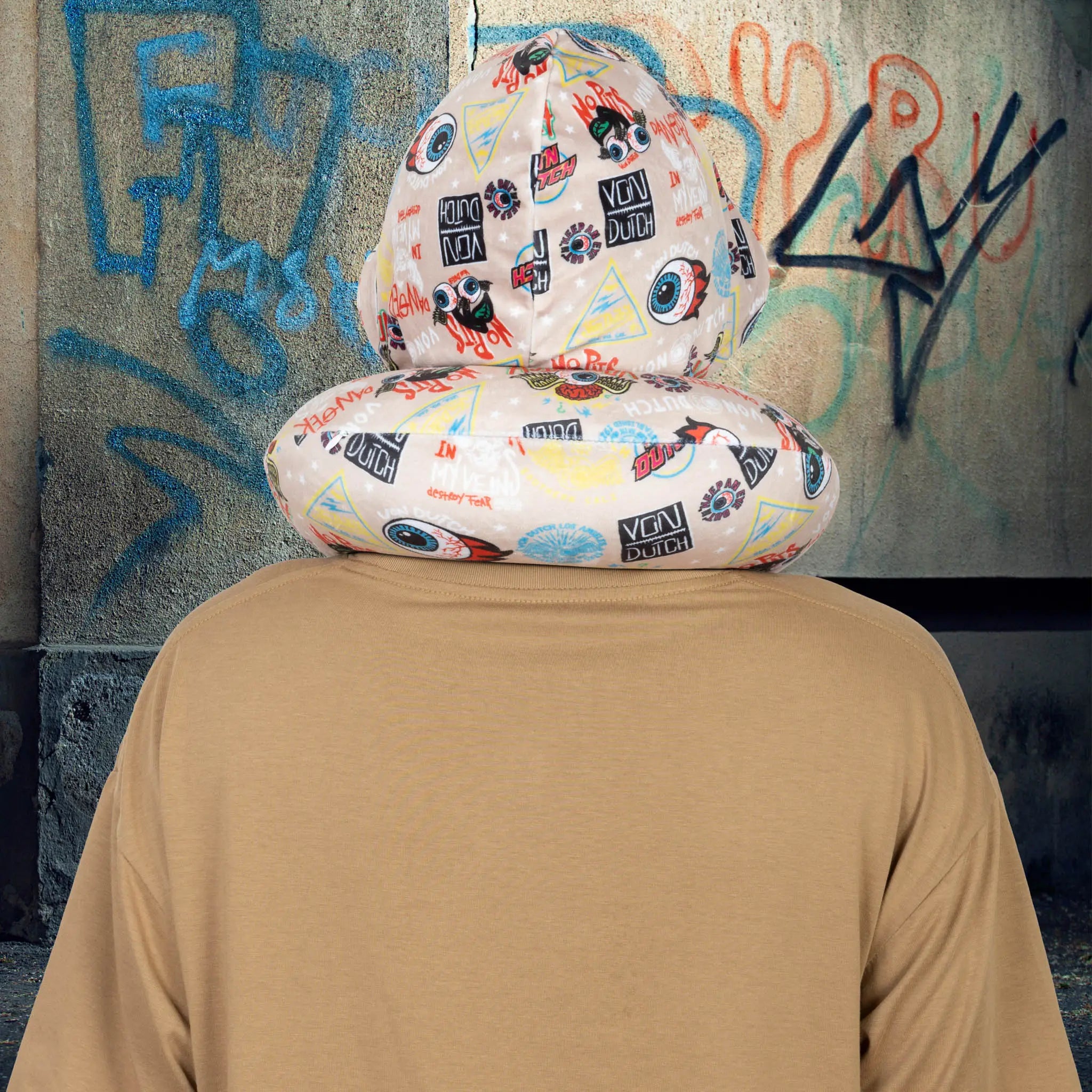 Person wearing a colorful patterned seat cover over their head against a graffiti-covered wall.