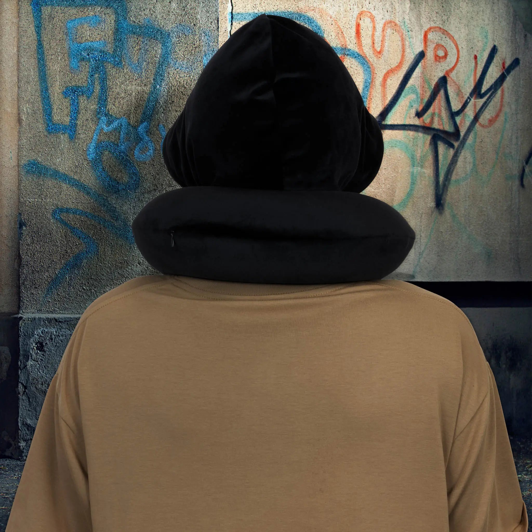 Person wearing a black hooded garment in front of a graffiti-covered wall