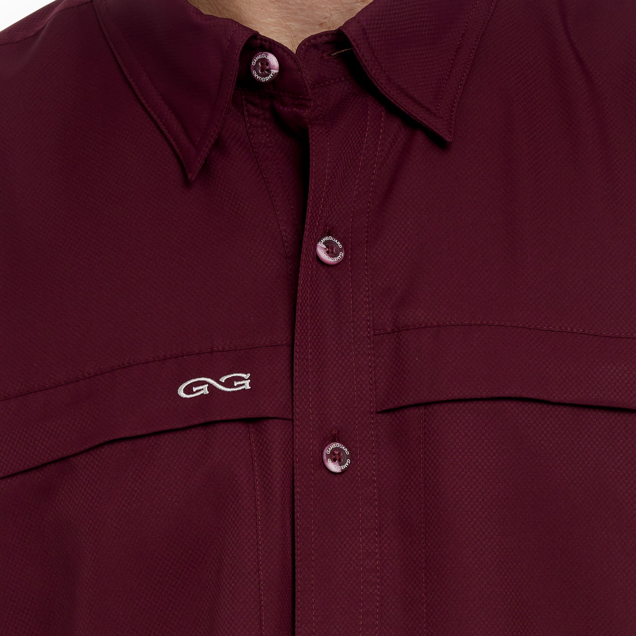 Close-up of a maroon shirt with button details and a logo on a plain background