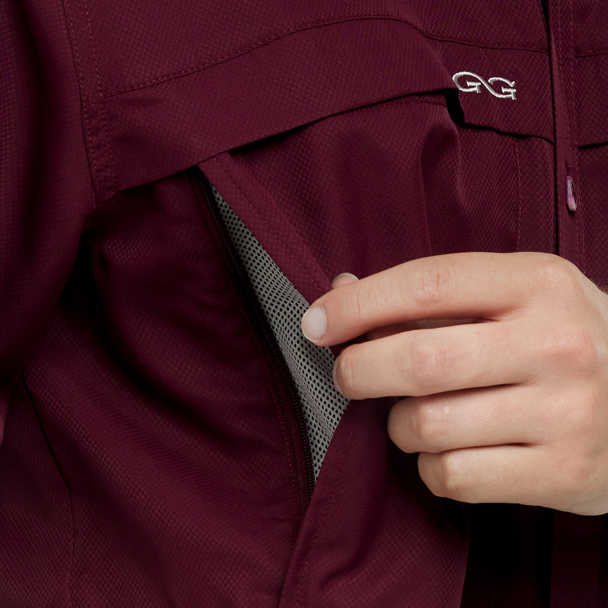 Close-up of a maroon jacket with a hand adjusting the hood, featuring a brand logo.