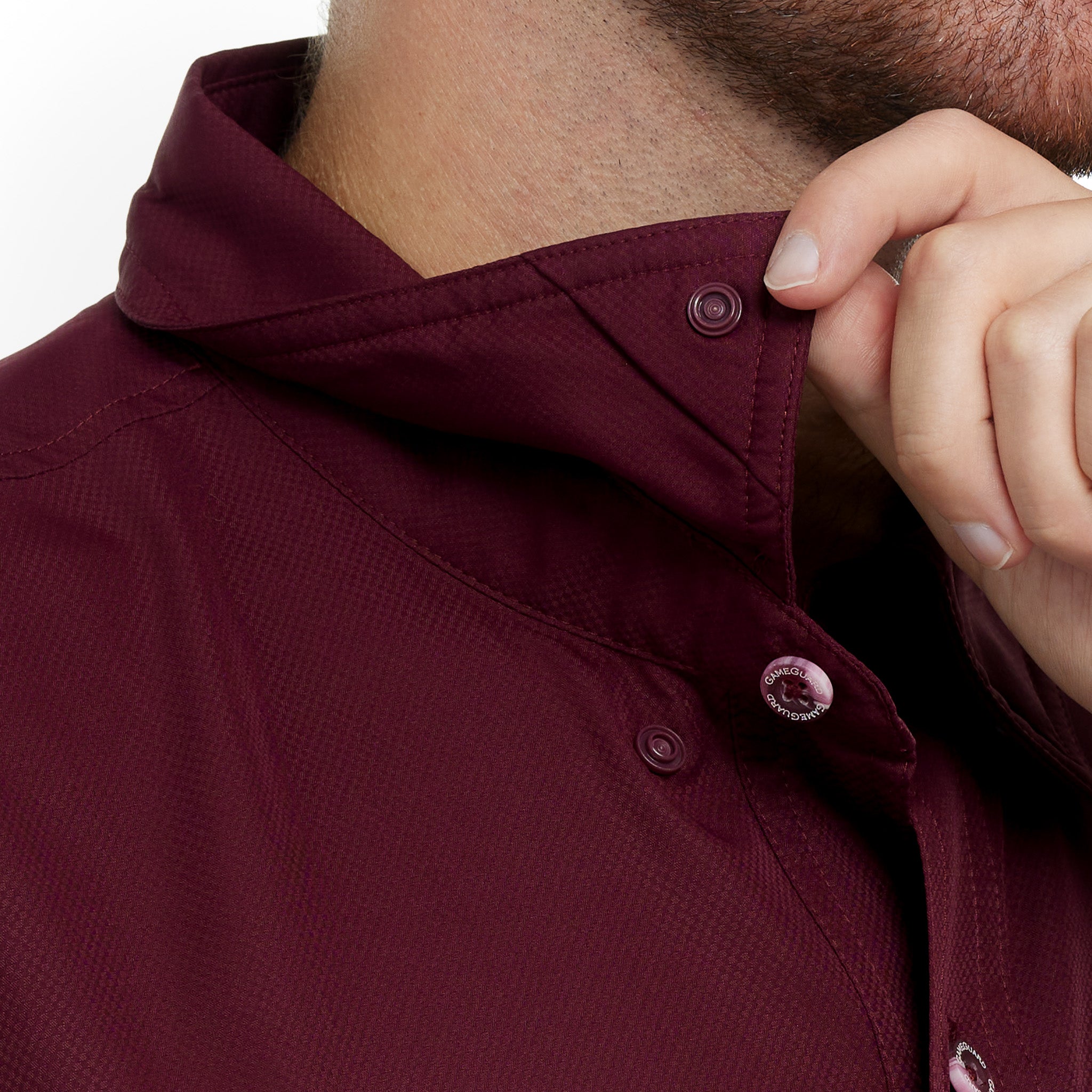 Close-up of a maroon shirt with buttons being adjusted on a white background