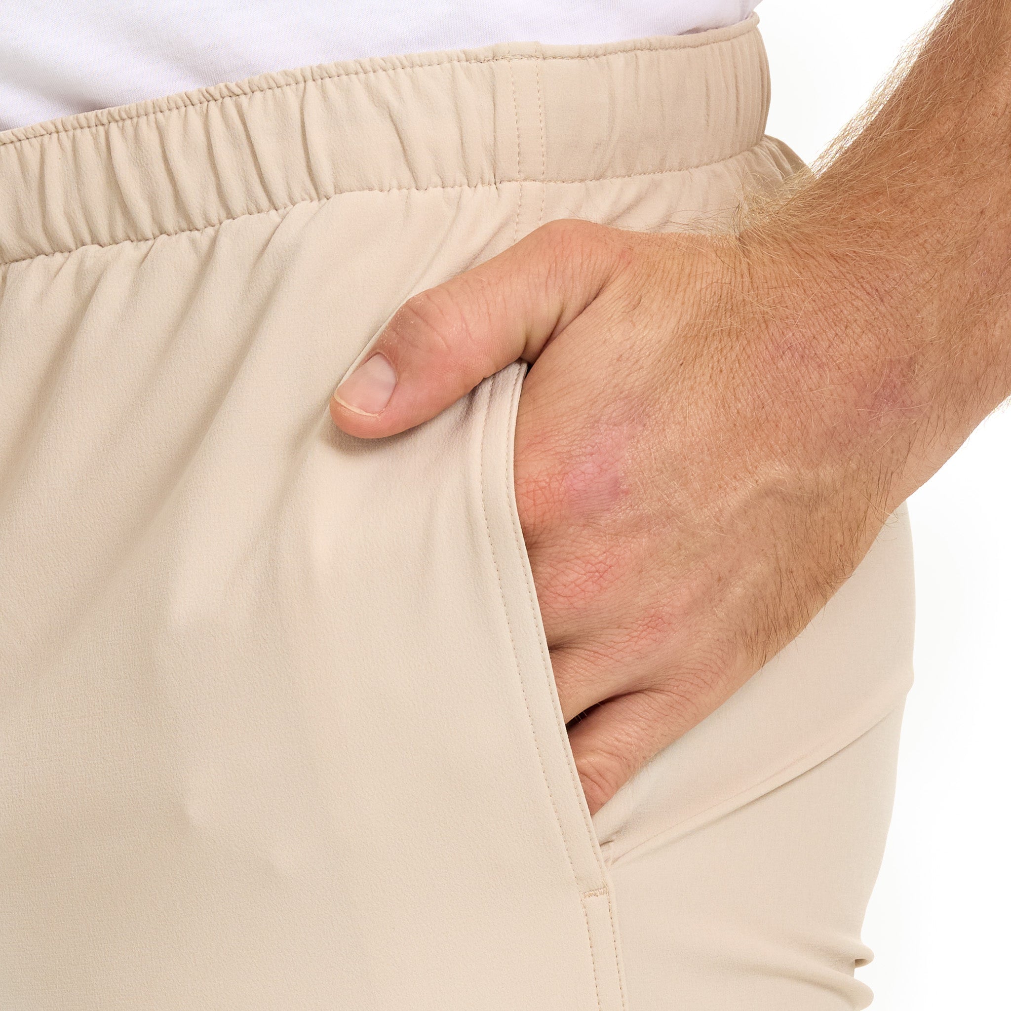 Close-up of a person wearing beige shorts with a hand adjusting the waistband on a white background.