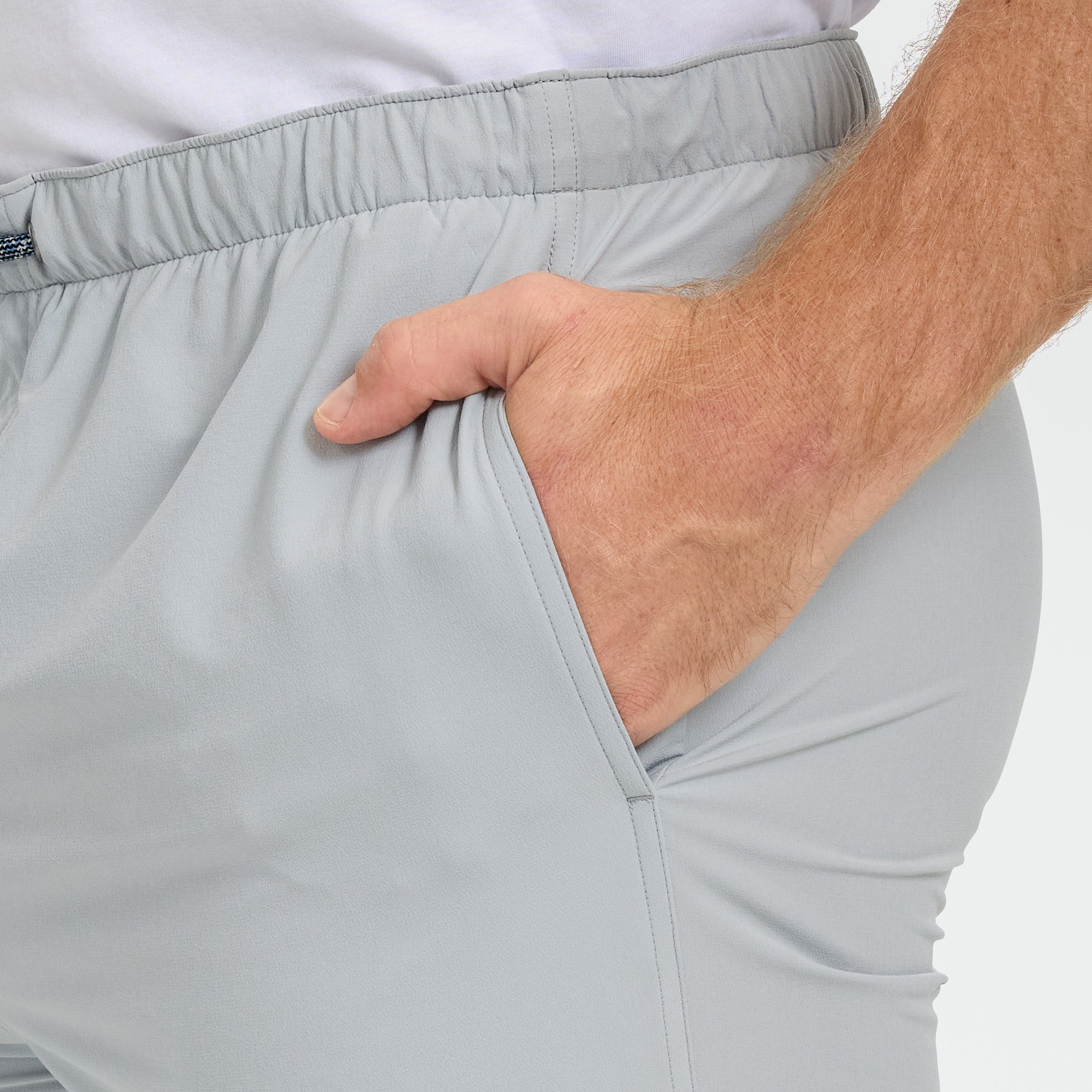 Close-up of a person wearing light gray shorts with a hand adjusting the waistband.