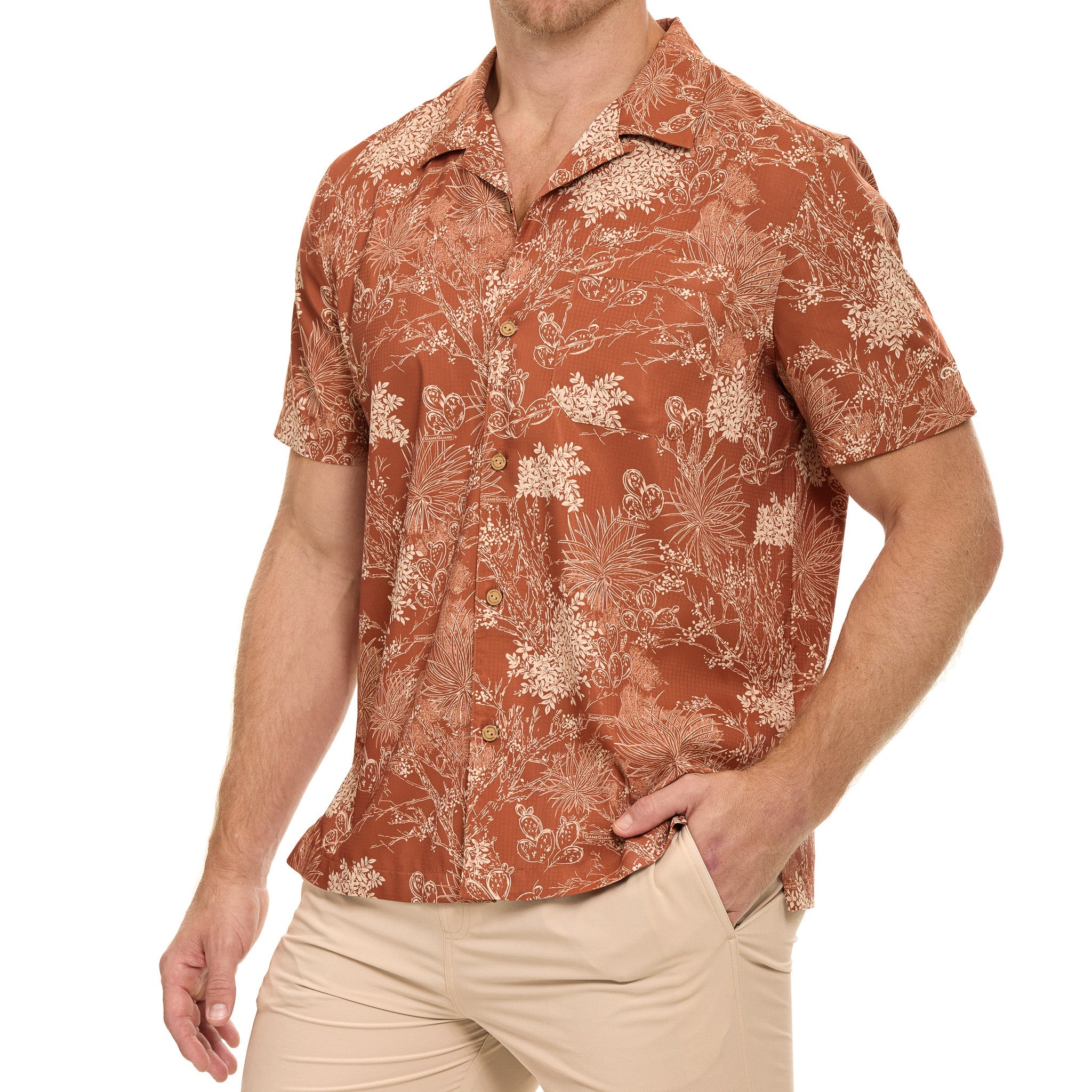 A man wearing a short-sleeve button-up camp shirt in rust orange with a beige botanical pattern, paired with khaki pants, against a plain white background.