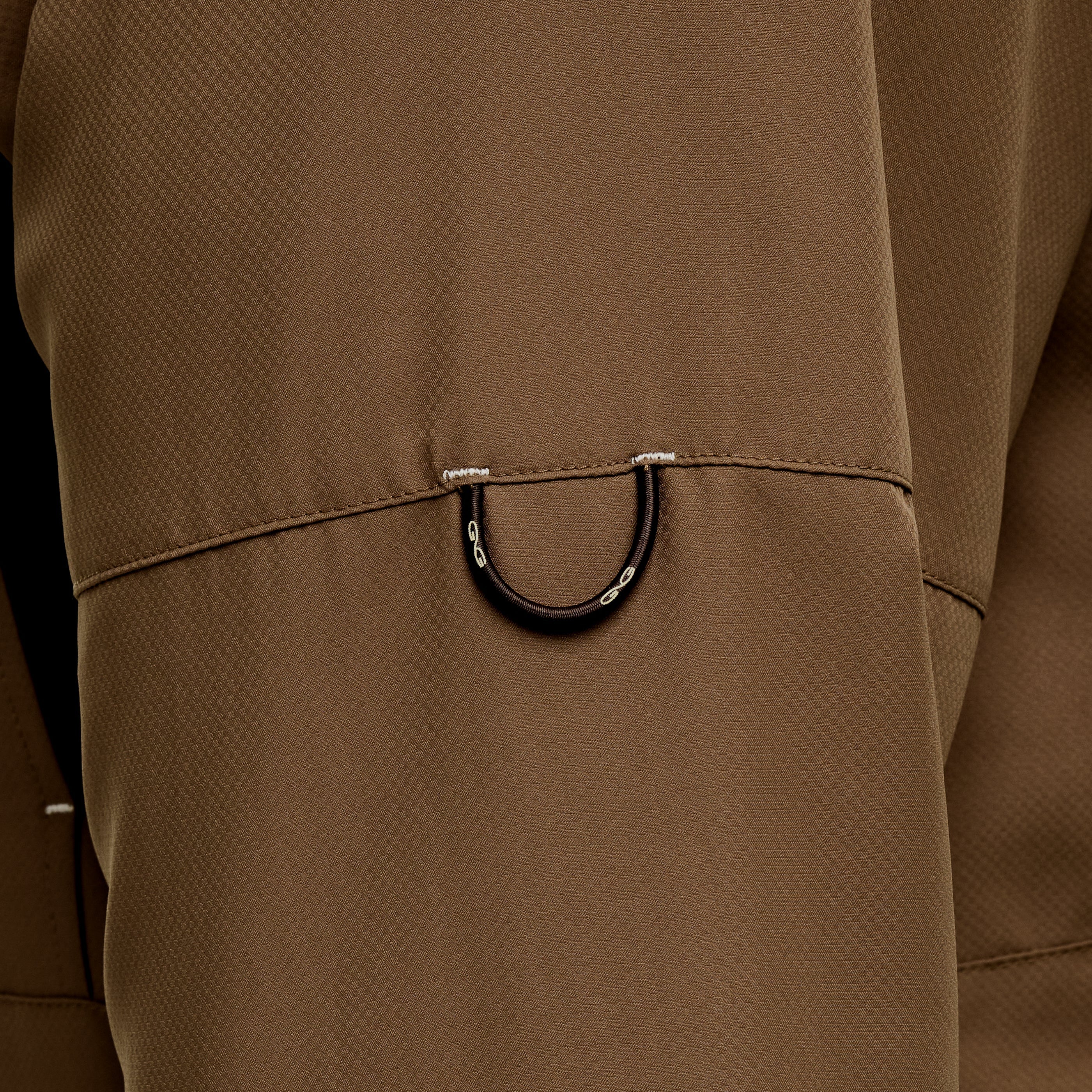 Close-up of a brown textured jacket featuring a black D-ring detail on the chest pocket.