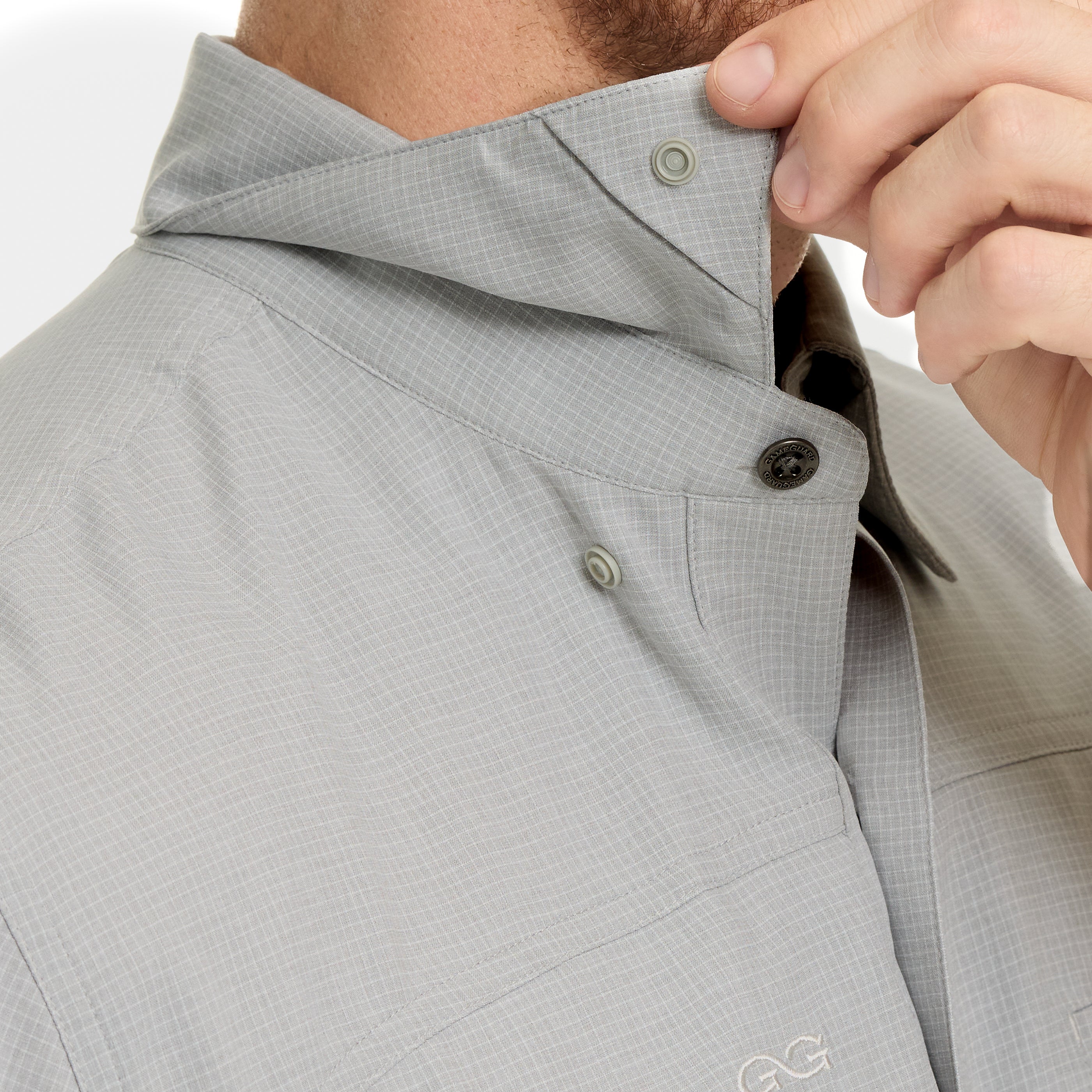 Close-up of a person adjusting the collar of a gray shirt with a visible brand logo.