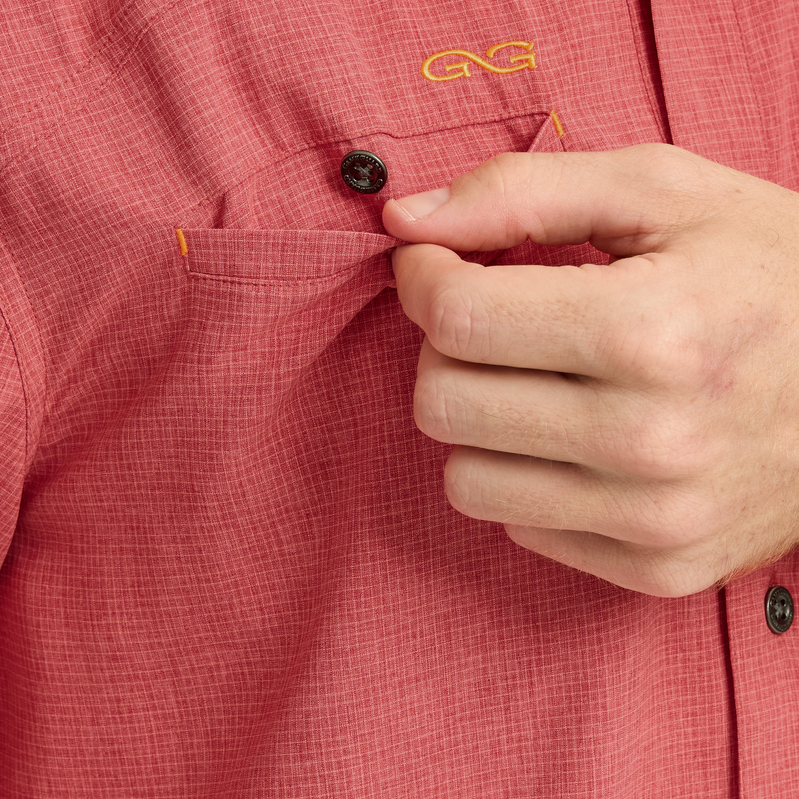 Close-up of a hand buttoning a red shirt with a brand logo.