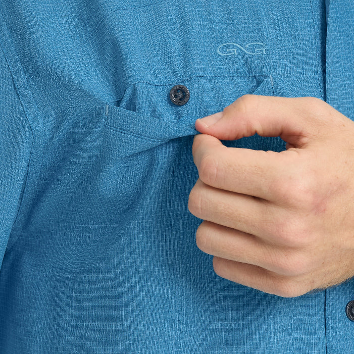 Close-up of a hand buttoning a blue shirt with a brand logo.